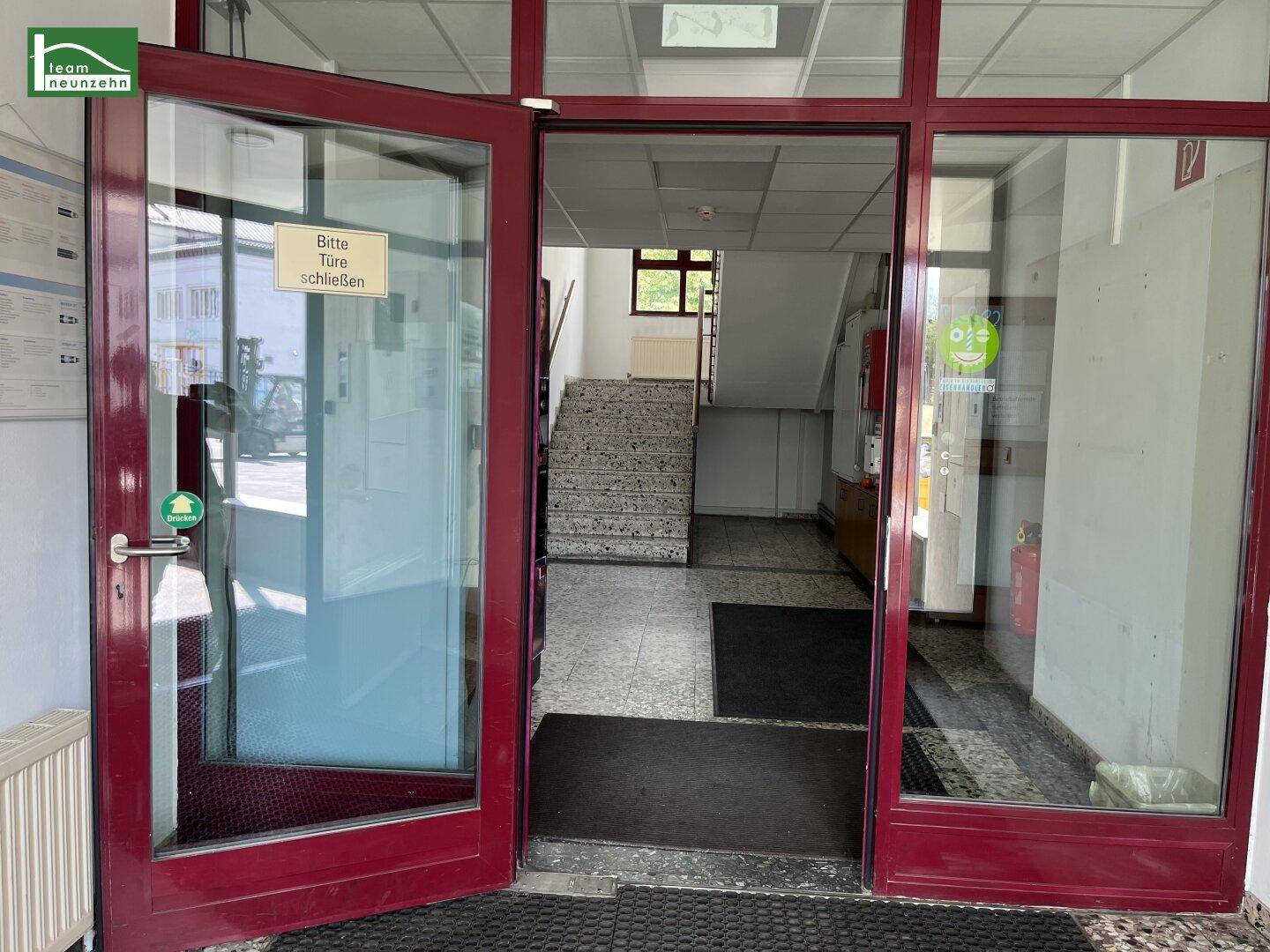 Eingangsbereich mit Glastür, Treppenhaus und Fliesenboden, der zum Obergeschoss führt.