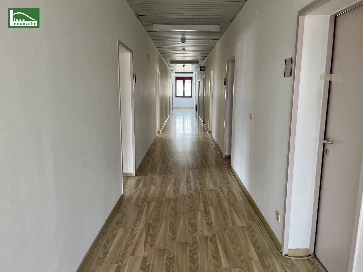 Langer Flur mit Holzoptik-Laminatboden, weißen Wänden und Deckenpaneelen.