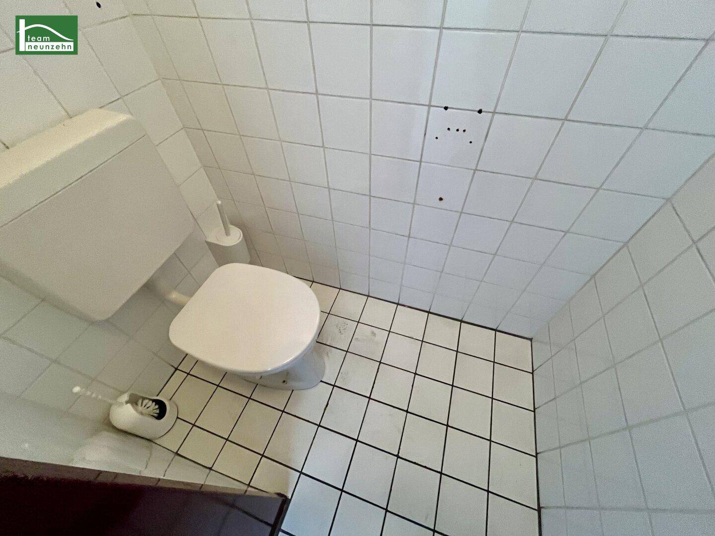 Kleine Toilette mit weißen Fliesen an Wänden und Boden sowie einem WC.