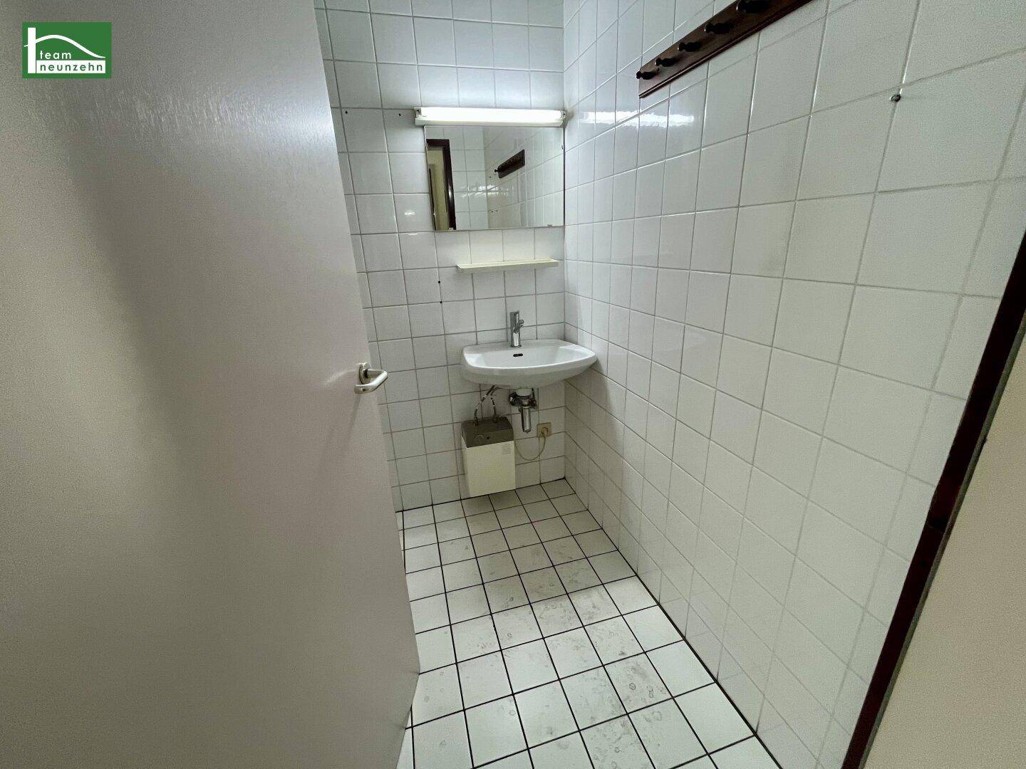 Badezimmer mit weißen Fliesen, Waschbecken und Spiegel, in gutem Zustand.