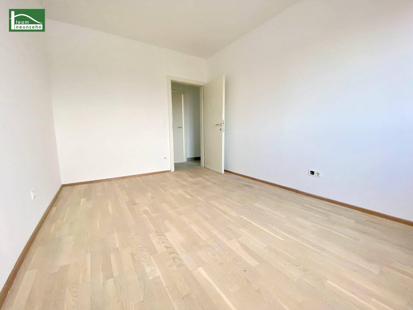 Geräumiges Zimmer mit hellem Parkettboden und Zugang zu weiteren Räumen.