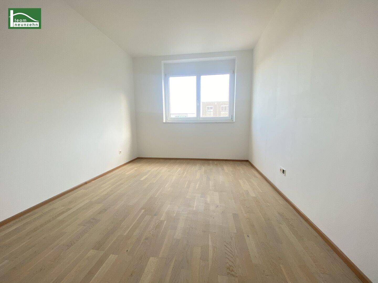 Geräumiges Schlafzimmer mit hellem Parkettboden und großem Fenster.