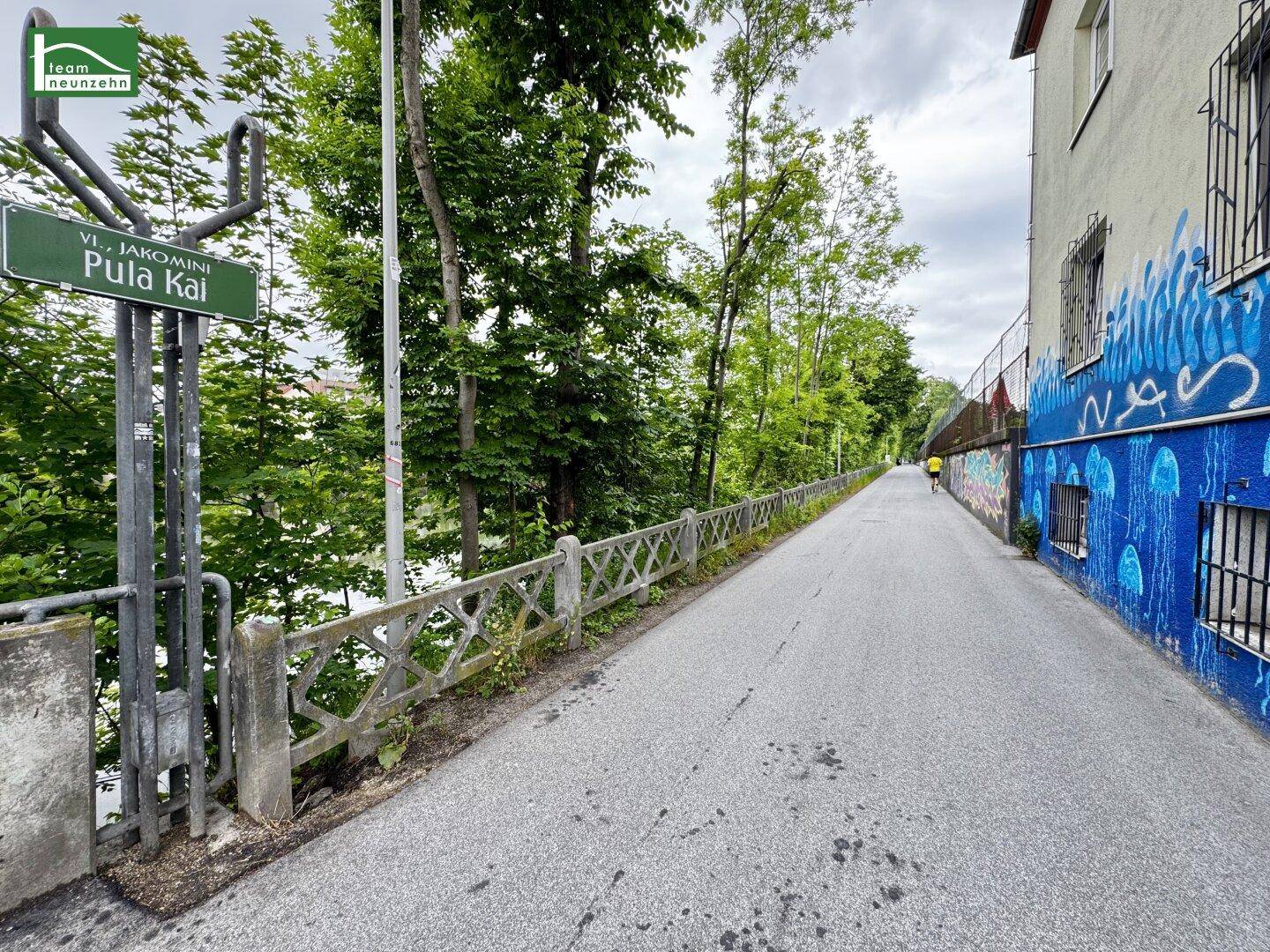 Ruhige Straße mit viel Grün und einem Gebäude mit farbenfroher Wandmalerei.