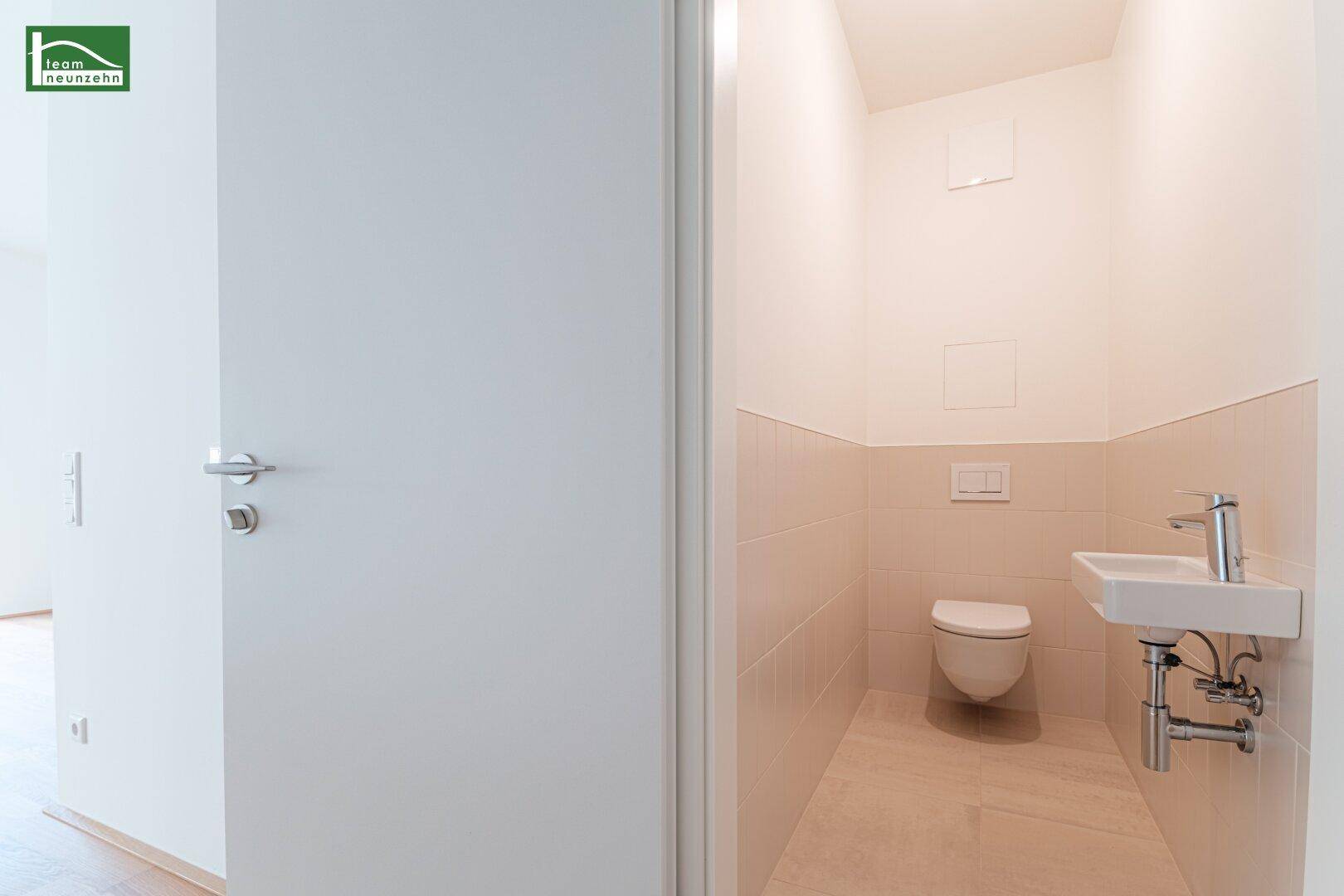 Separates Gäste-WC mit hellbeigen Fliesen, wandhängender Toilette und kleinem Waschbecken.