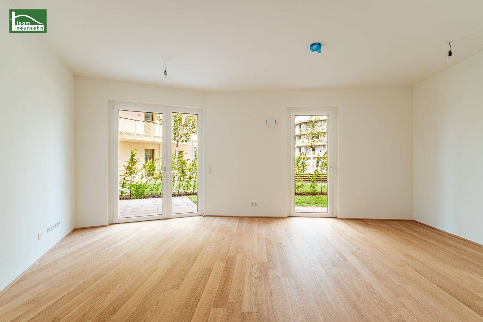 Heller, leerer Raum mit Parkettboden und großen Glastüren, die zu einer Terrasse führen.