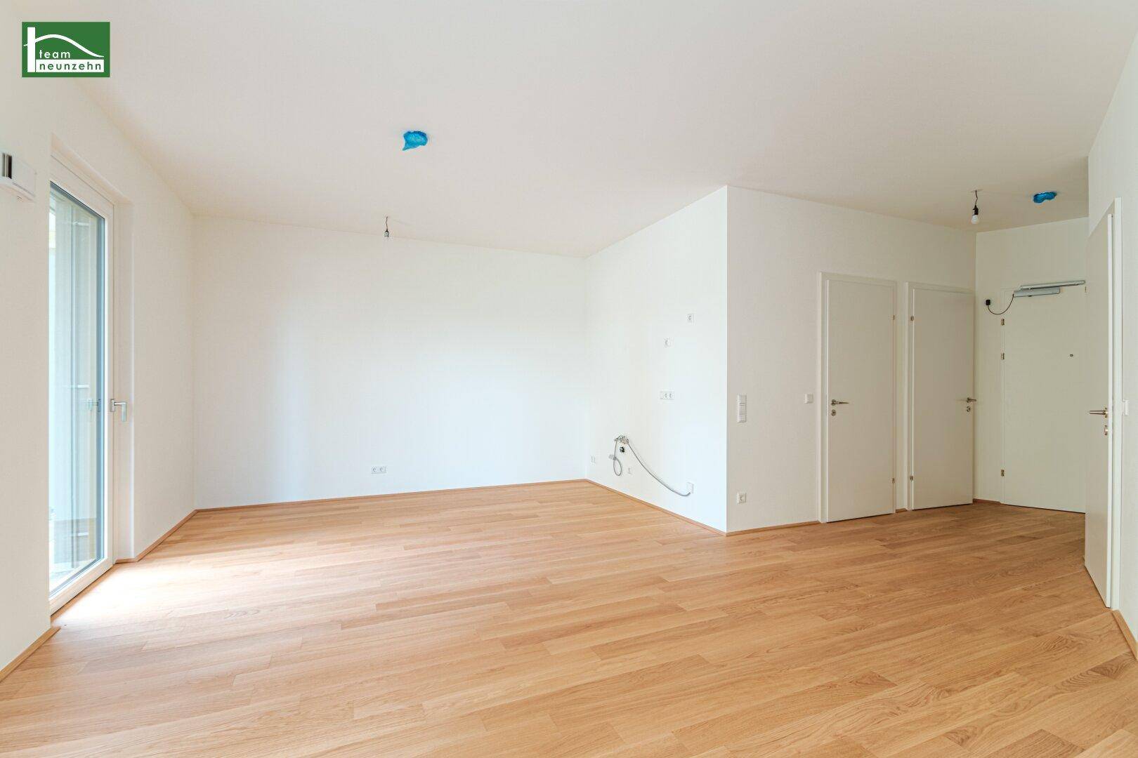 Geräumiger, leerer Wohnbereich mit Holzboden und viel Tageslicht durch große Fenster und Türen.