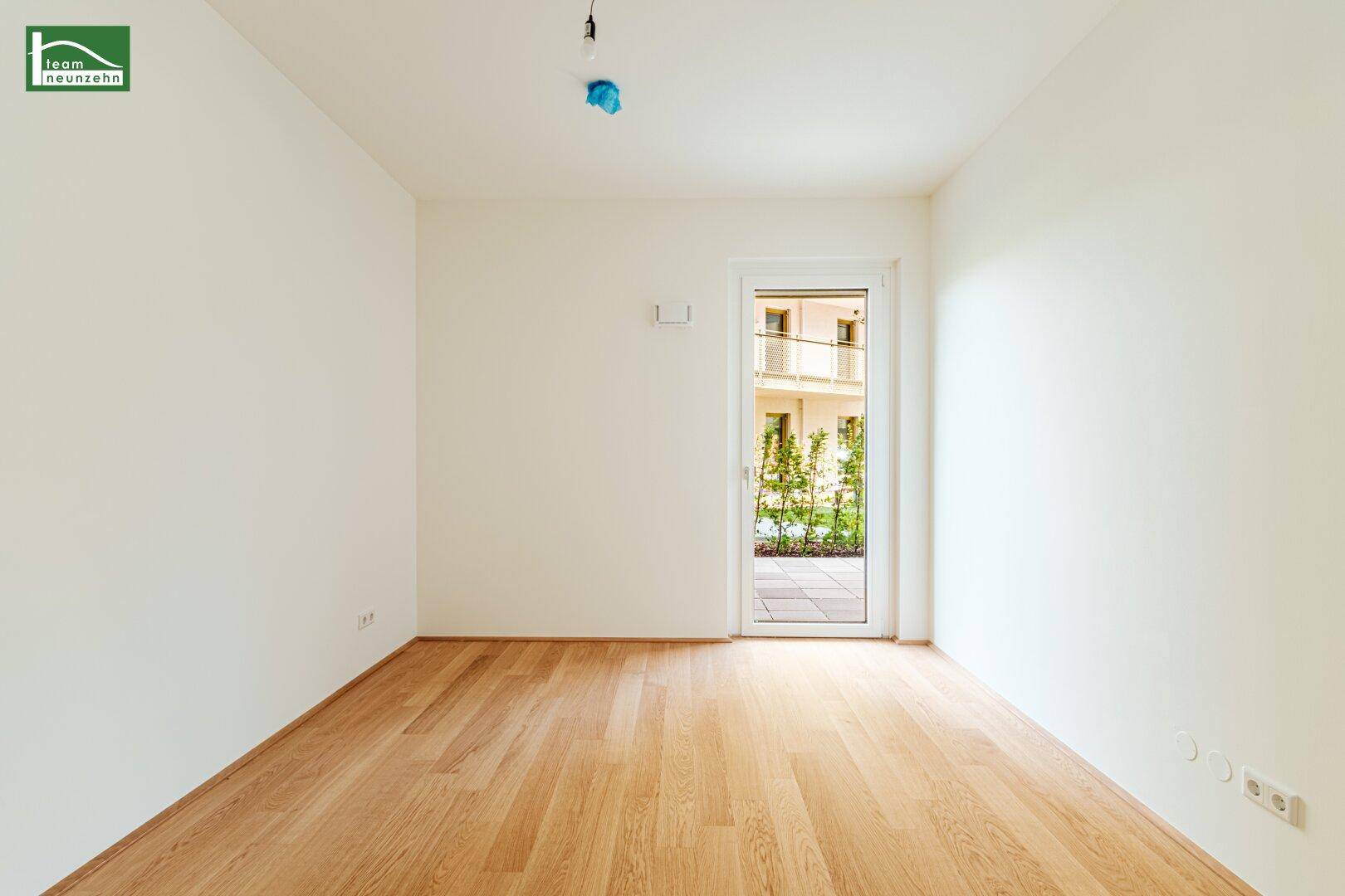 Heller, leerer Raum mit Holzboden und Zugang zu einer Terrasse oder Garten im Erdgeschoss.
