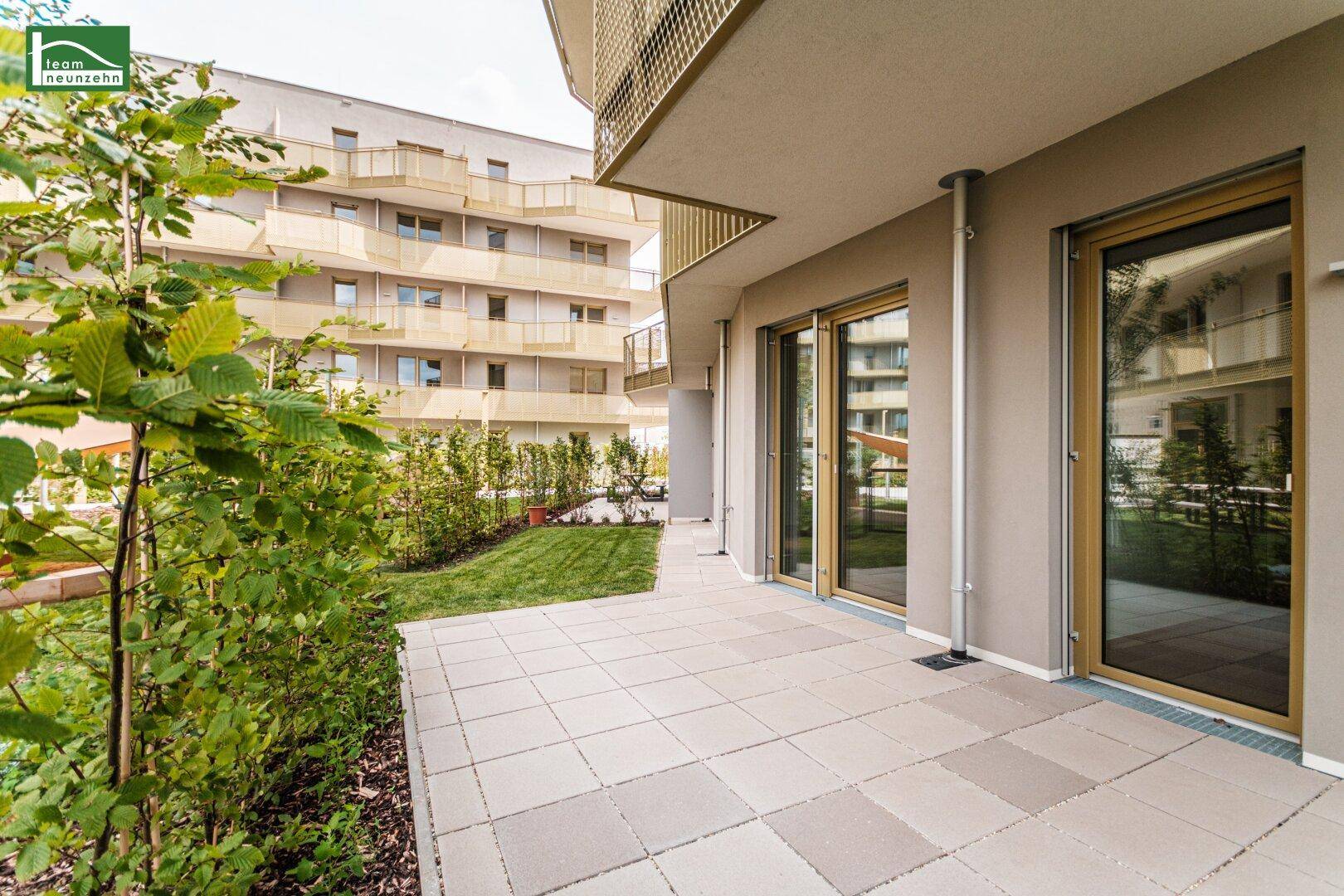 Geräumige Terrasse mit angrenzender Rasenfläche und Blick auf die moderne Wohnanlage.