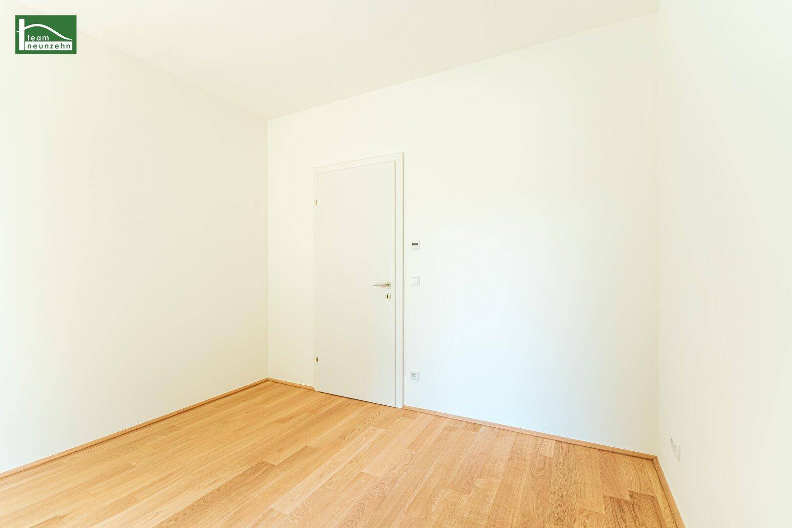 Helles, leeres Zimmer mit Parkettboden und weißer Tür, ideal als Schlafzimmer.