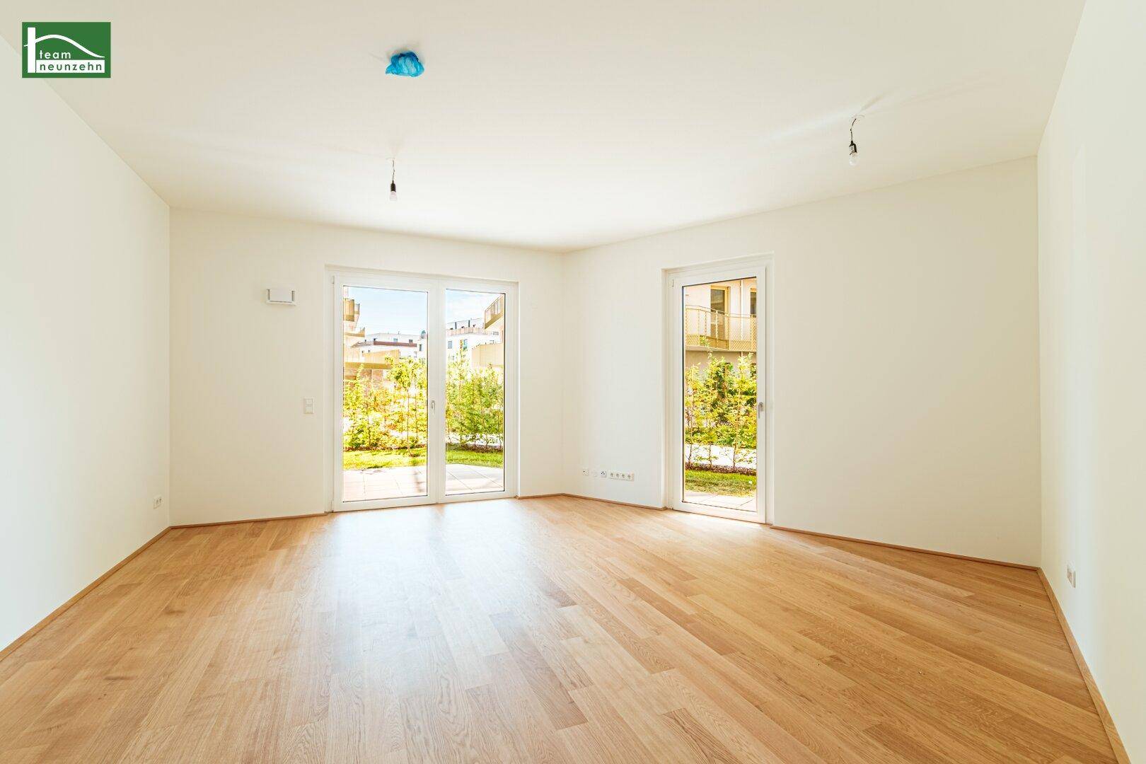 Helles, leeres Wohnzimmer mit Parkettboden und Zugang zum Gartenbereich.