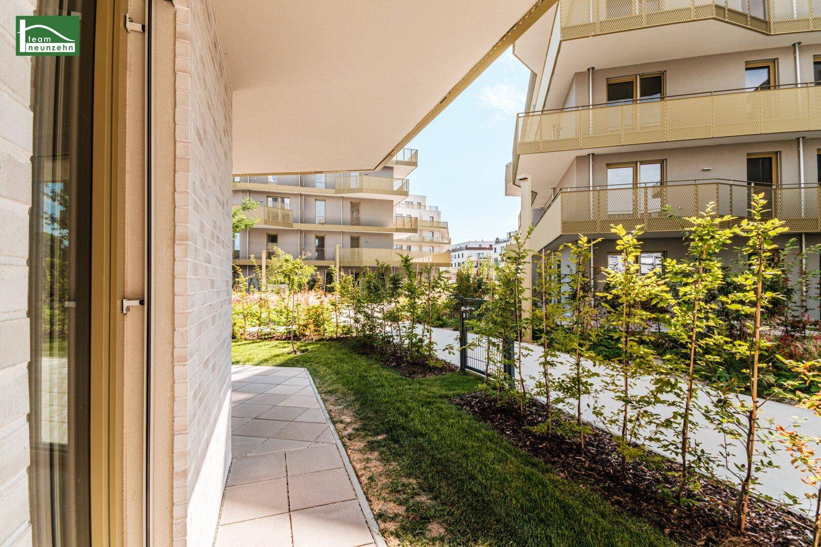Gepflegter Gartenbereich mit Terrasse und junger Bepflanzung vor der modernen Wohnanlage.