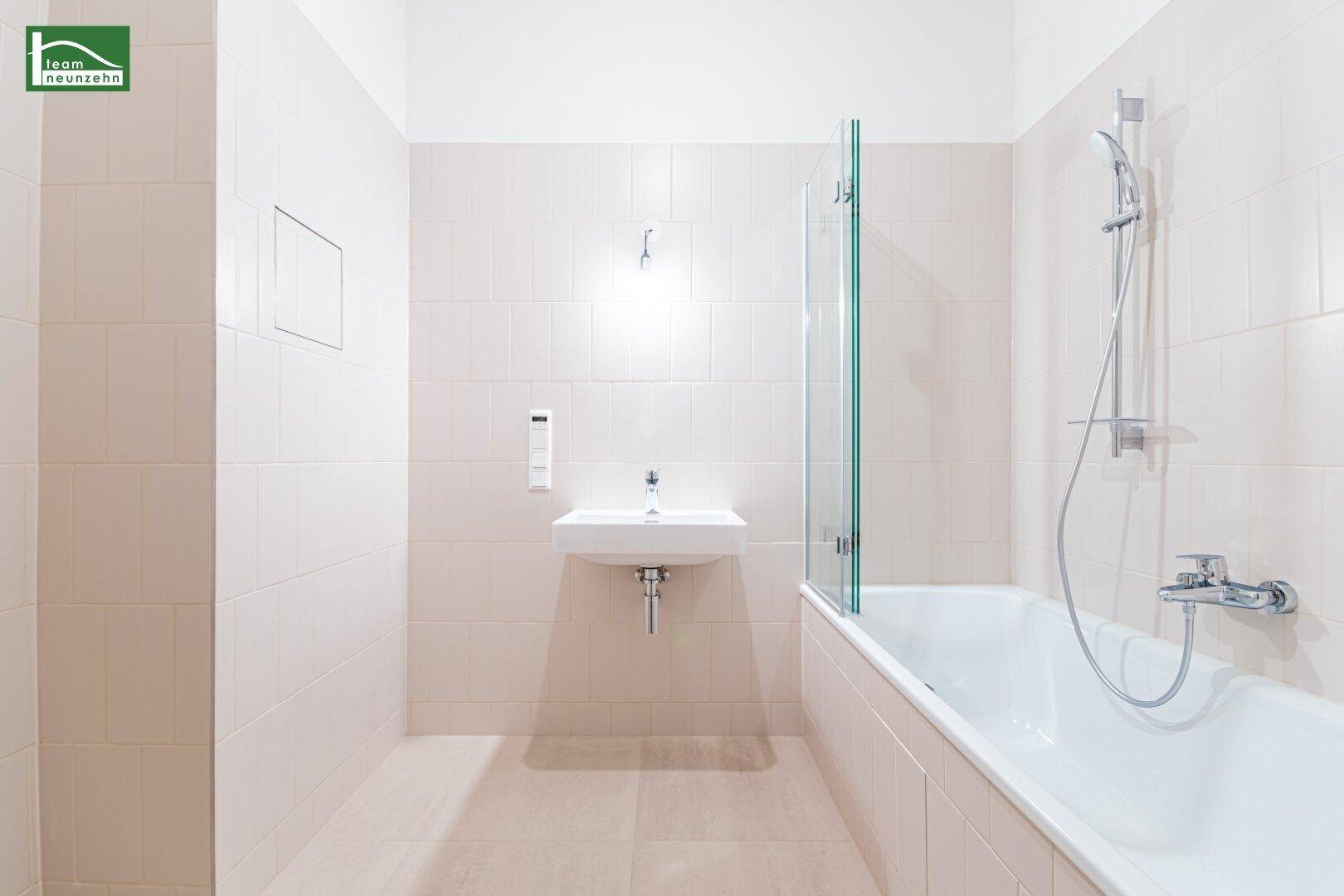 Modernes Badezimmer mit hellen Fliesen, Badewanne mit Duschwand und Einzelwaschbecken.