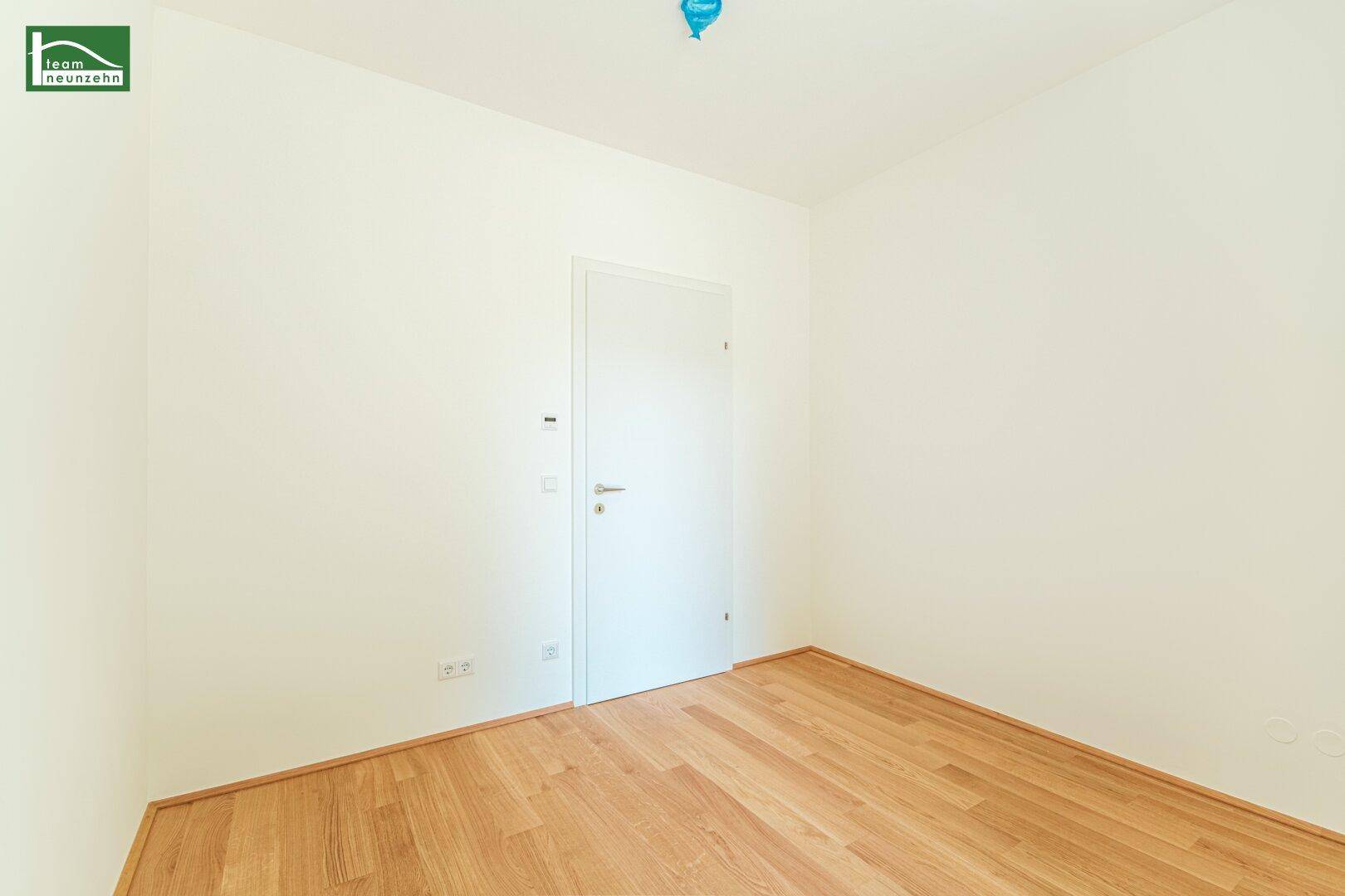Unmöbliertes Zimmer mit hellem Holzfußboden und einer schlichten weißen Tür.