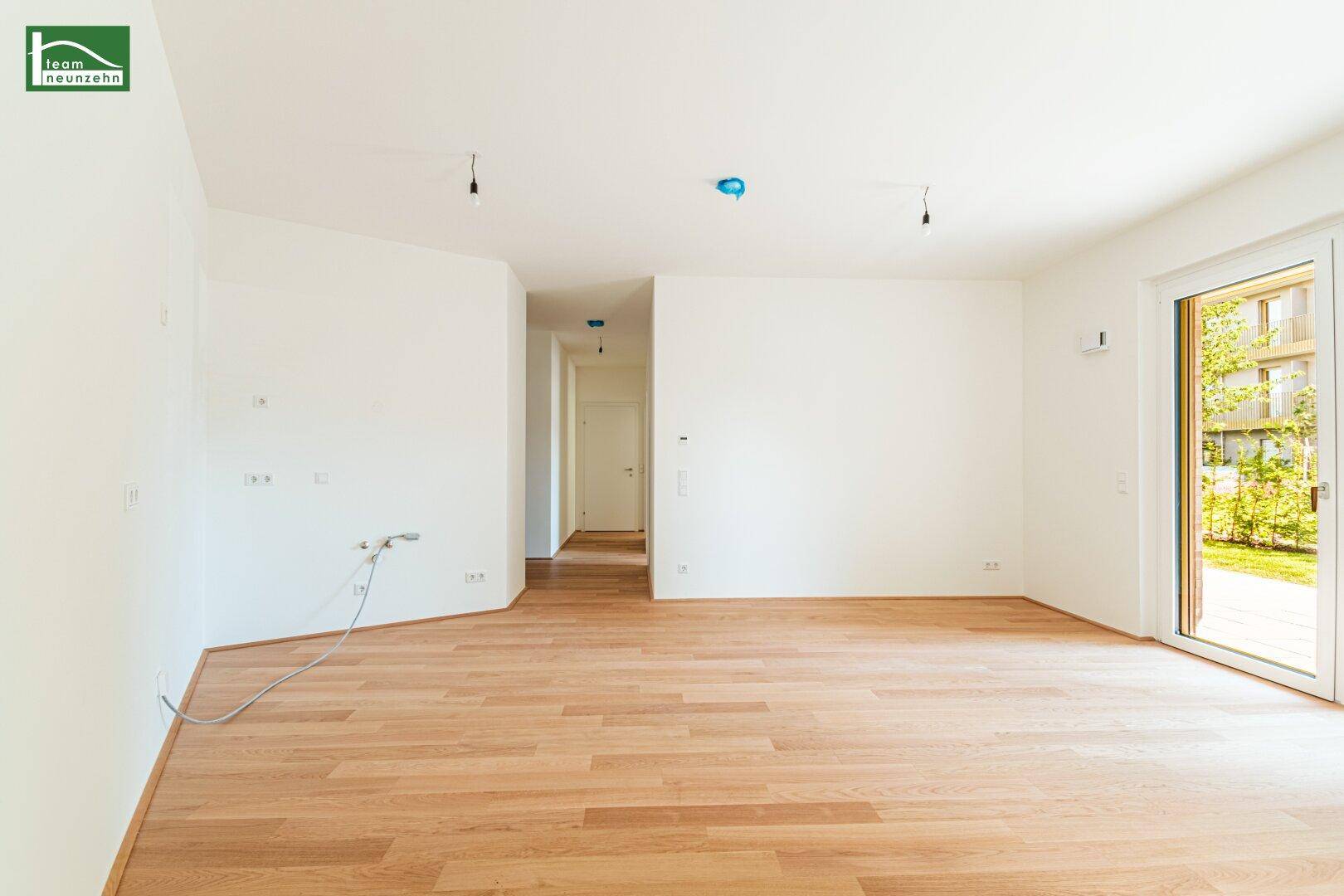 Geräumiges, unmöbliertes Zimmer mit hellem Parkettboden und Zugang zu einem Flur.