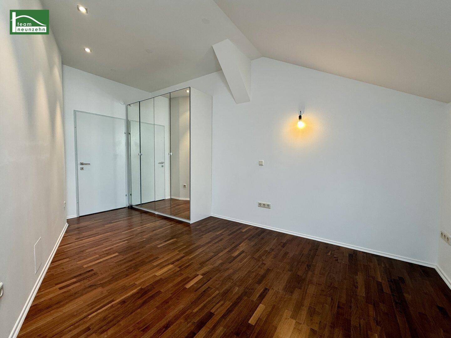 Leeres Schlafzimmer mit dunklem Parkettboden, Dachschräge und einem großen Spiegelschrank.