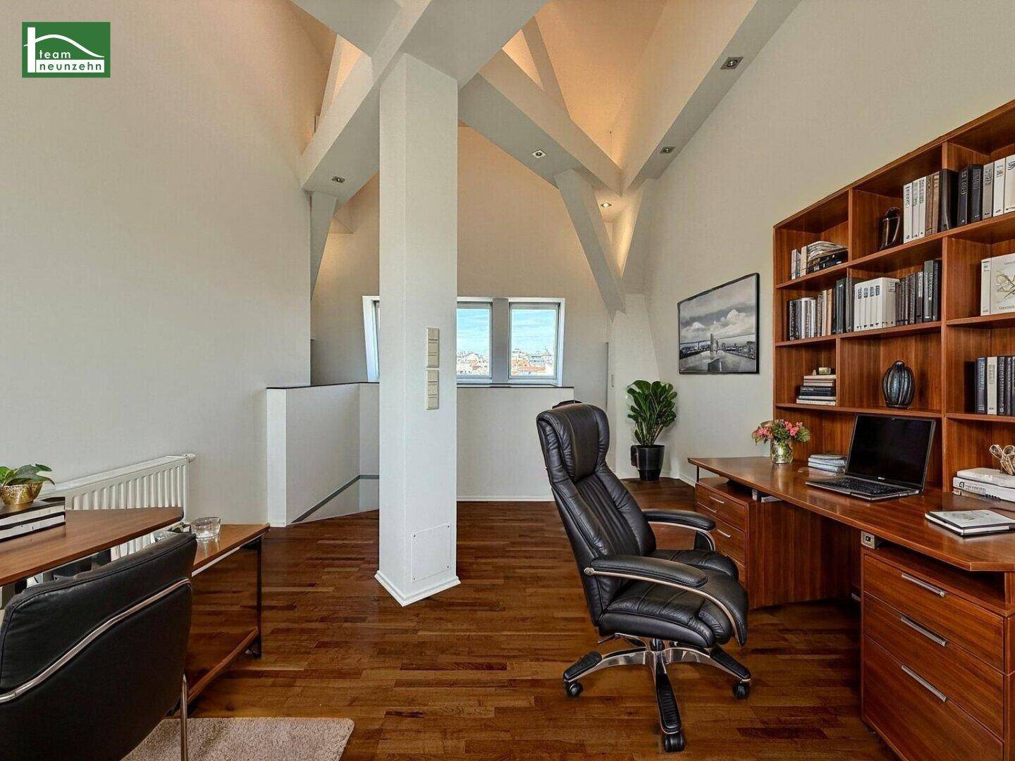 Helles Arbeitszimmer im Dachgeschoss mit Holzboden, sichtbaren Balken und großem Bücherregal.