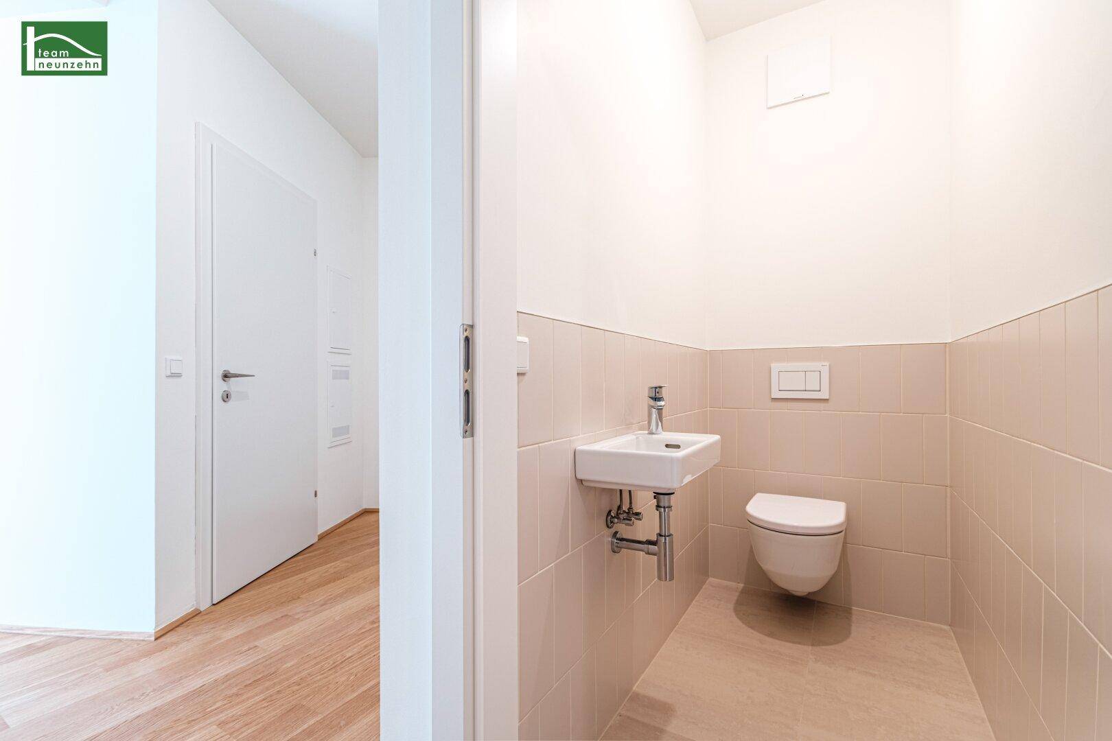 Separates Gäste-WC mit wandhängender Toilette und kleinem Waschbecken in hellen Fliesen.