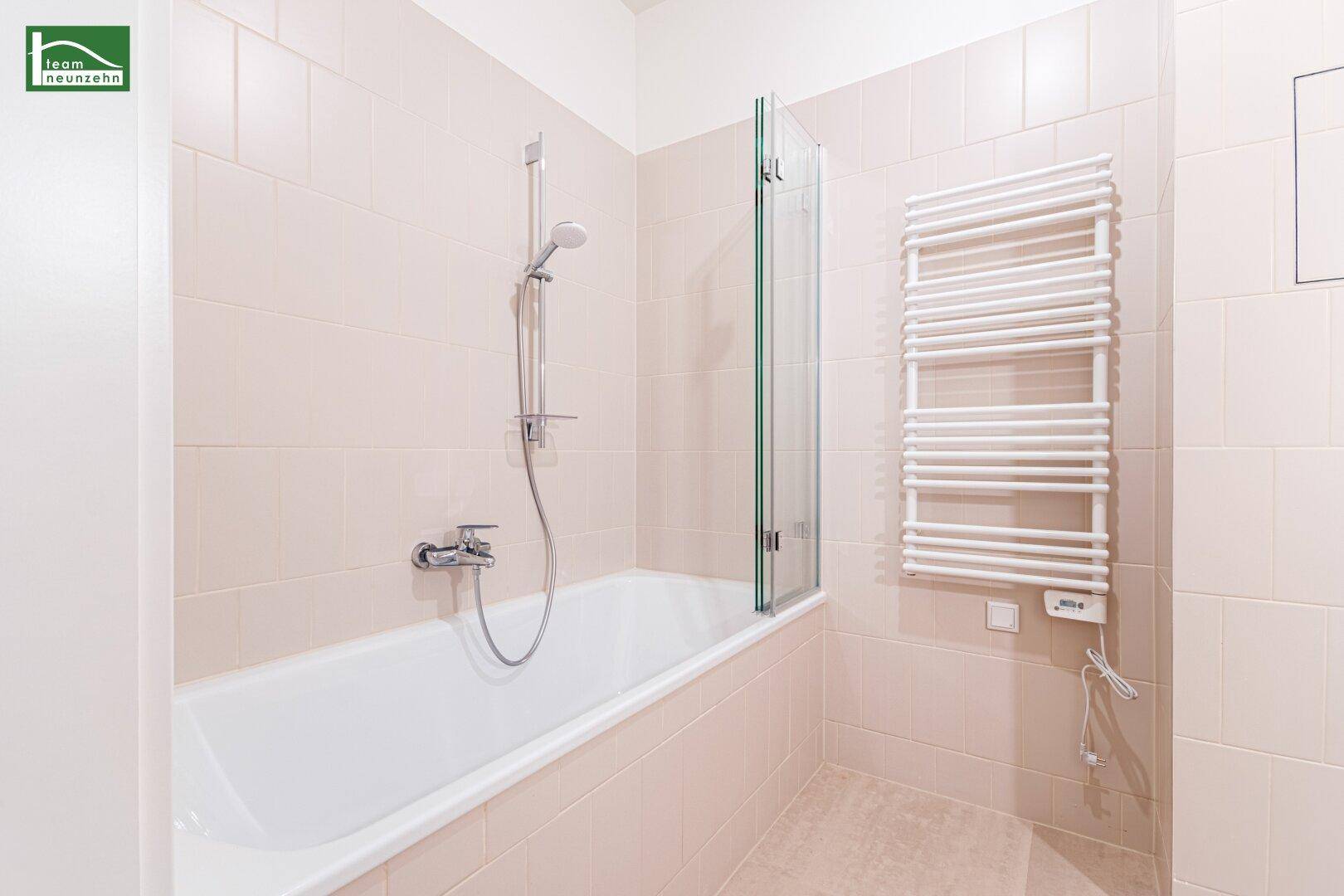 Modernes Badezimmer mit Badewanne, Duschfunktion und beheiztem Handtuchhalter in hellen Fliesen.