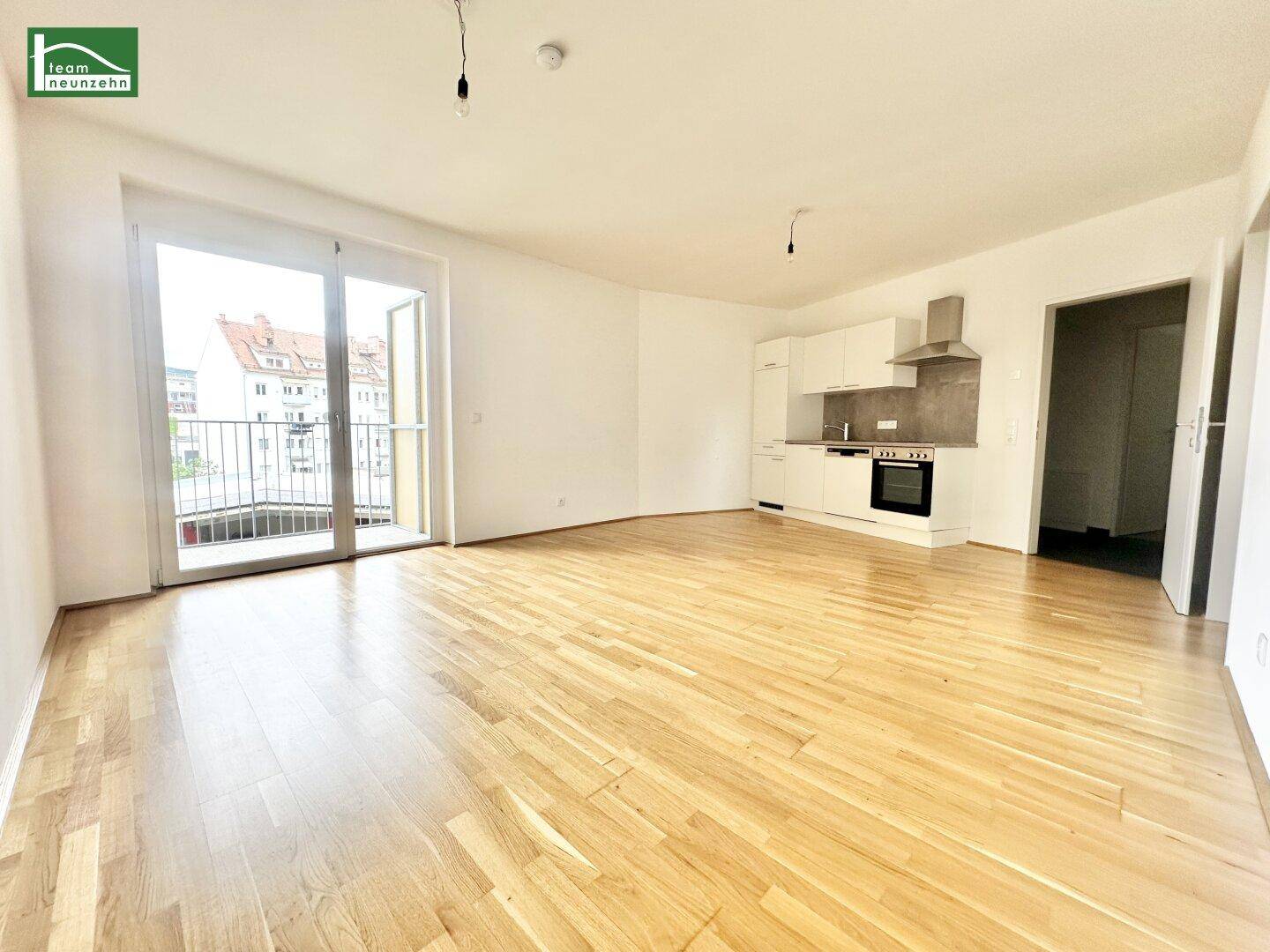 Lichtdurchfluteter Wohnbereich mit offener Küche, Parkettboden und Zugang zu einem Balkon.