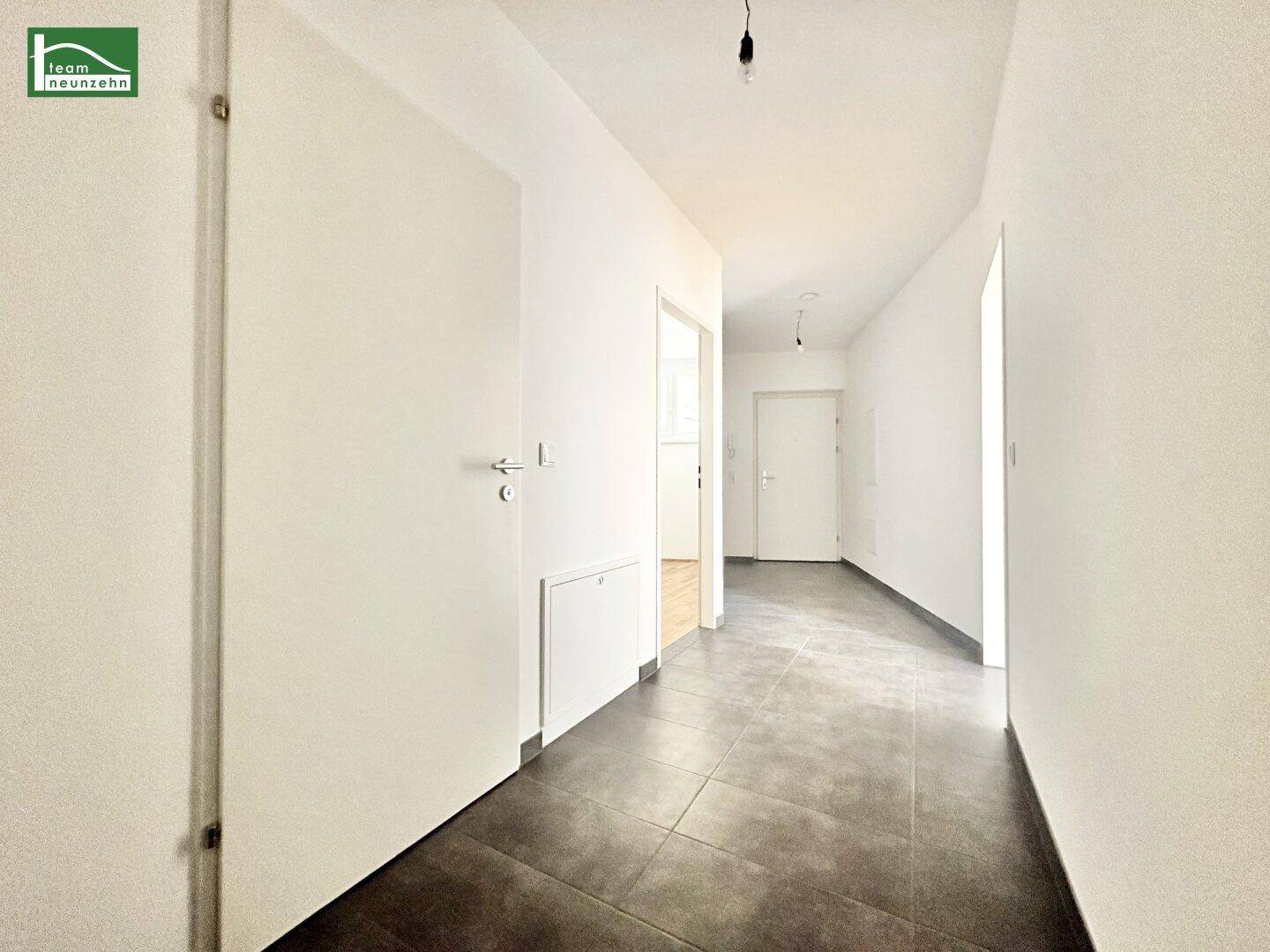 Geräumiger Flur mit dunklen Fliesen, weißen Wänden und mehreren Türen zu angrenzenden Räumen.