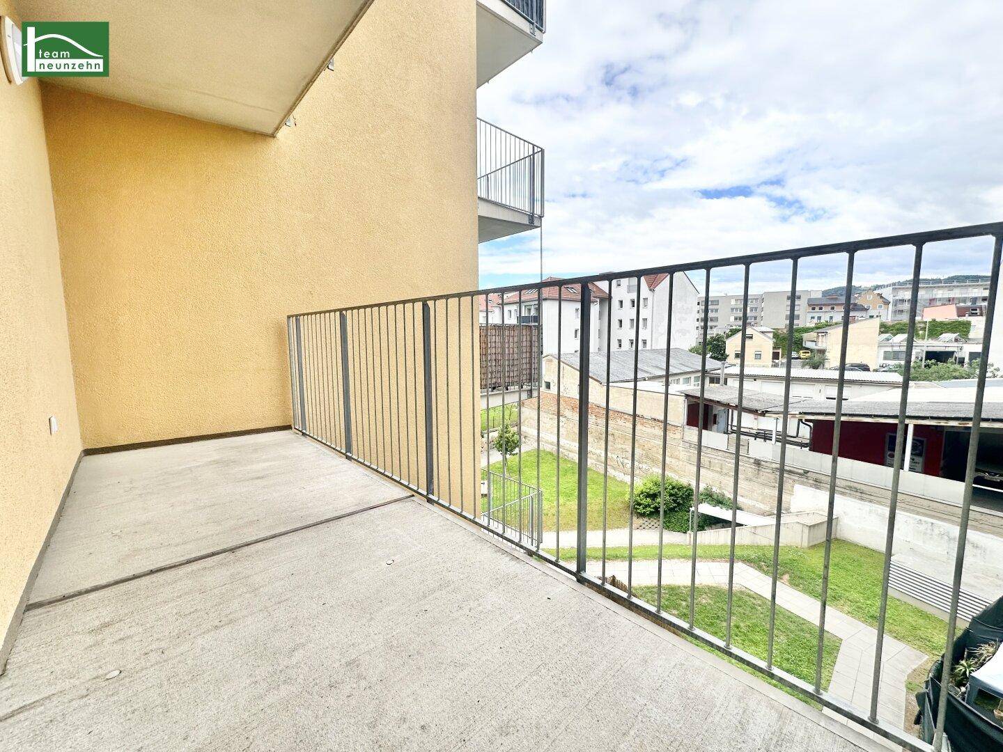 Geräumiger Balkon mit Betonboden und Metallgeländer, mit Blick auf einen begrünten Innenhof.