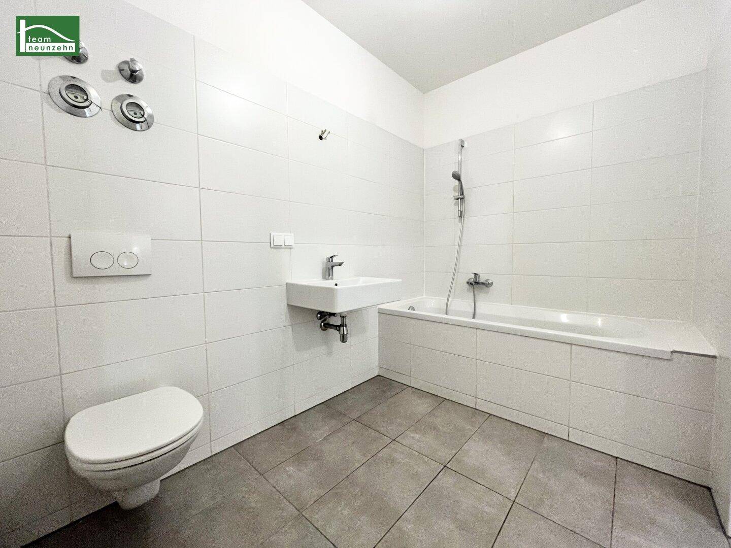 Modernes Badezimmer mit weißen Fliesen, Toilette, Waschbecken und Badewanne mit Duschfunktion.