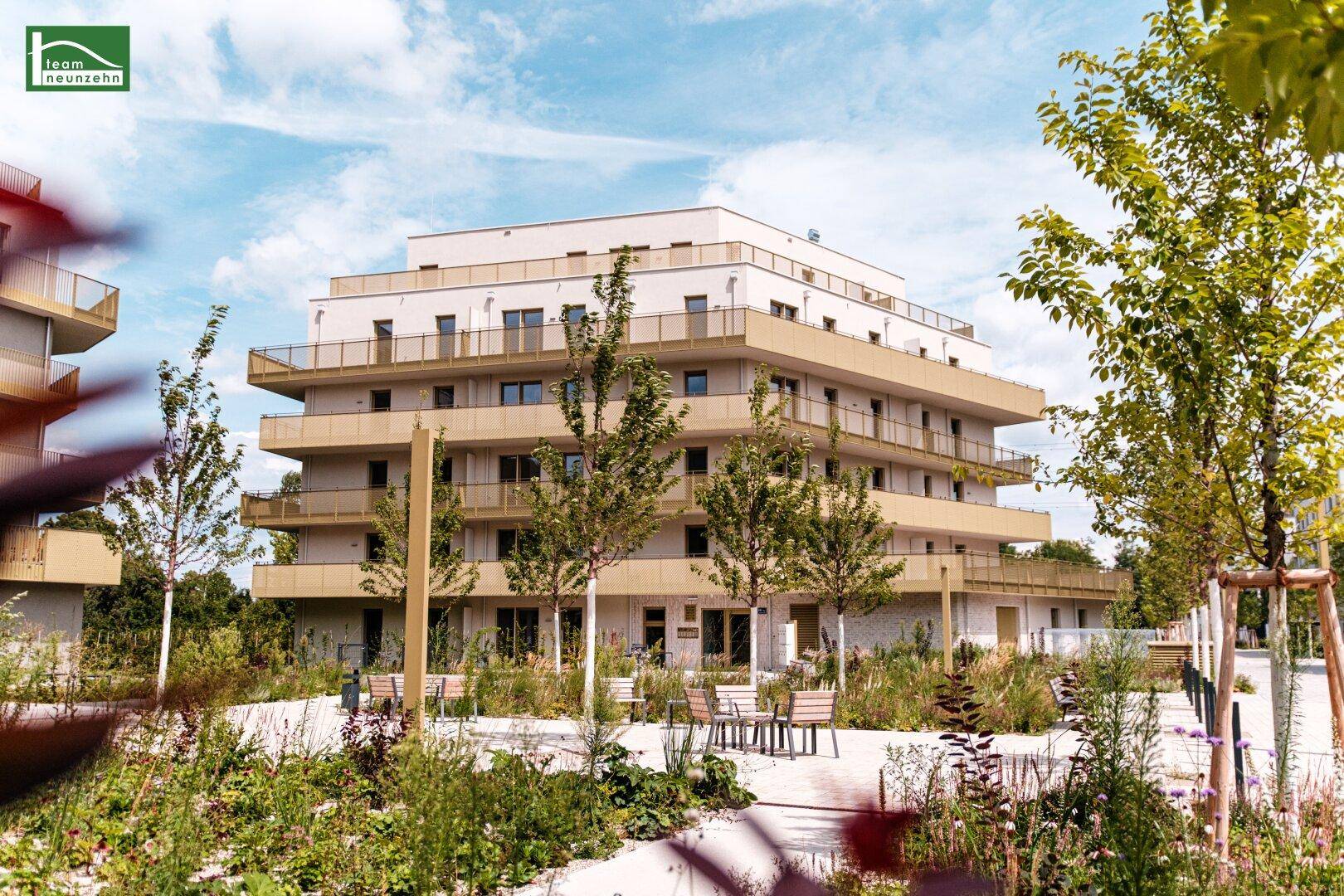 Modernes Apartmentgebäude mit vielen Balkonen und einer ansprechenden Außenanlage mit Sitzgelegenheiten.