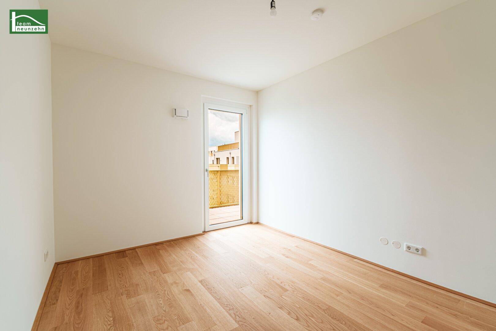 Helles Schlafzimmer mit Parkettboden und Zugang zu einem kleinen Balkon, ideal für frische Luft.