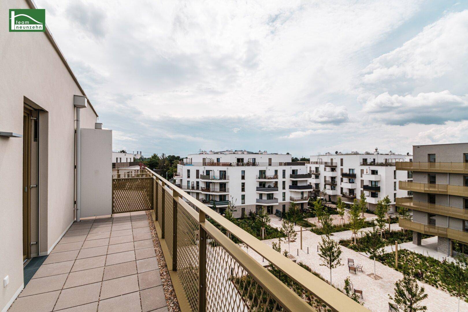 Langer Balkon mit Fliesenboden und weitem Blick über die moderne Wohnanlage und Grünflächen.