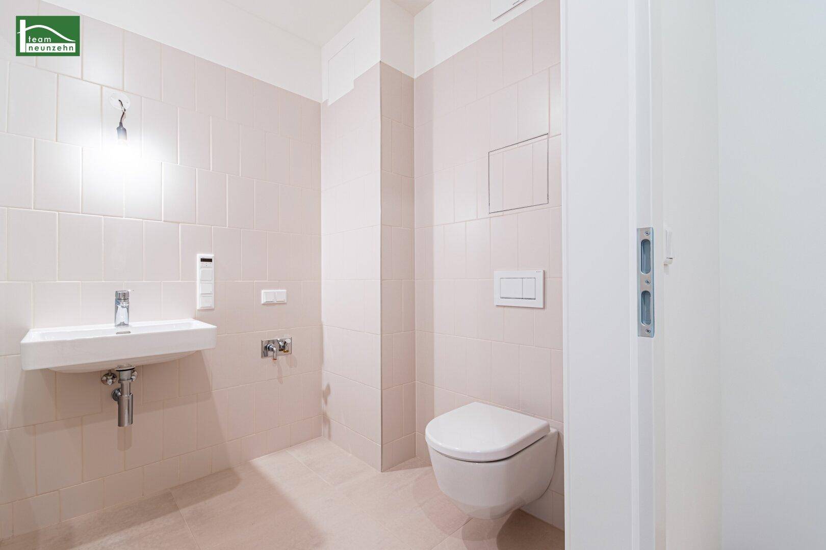 Helles WC mit wandhängender Toilette, Waschbecken und beigefarbenen Fliesen.