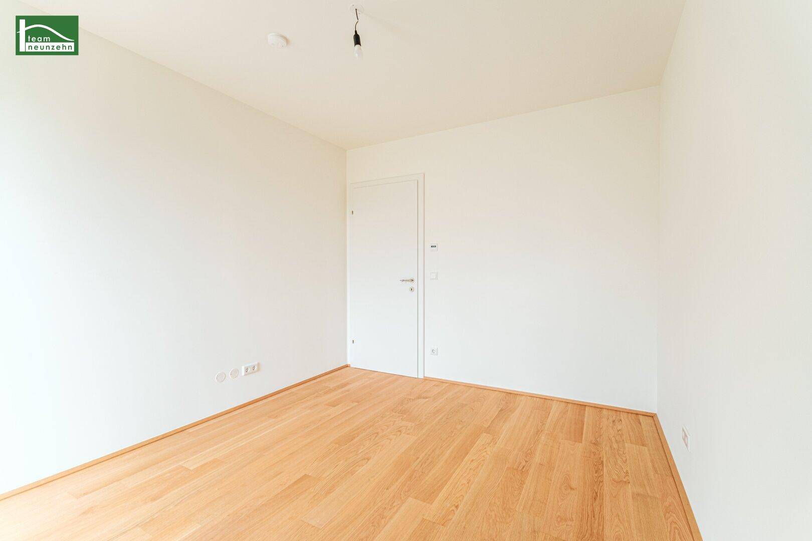 Unmöbliertes Zimmer mit hellem Holzboden und weiß gestrichenen Wänden.