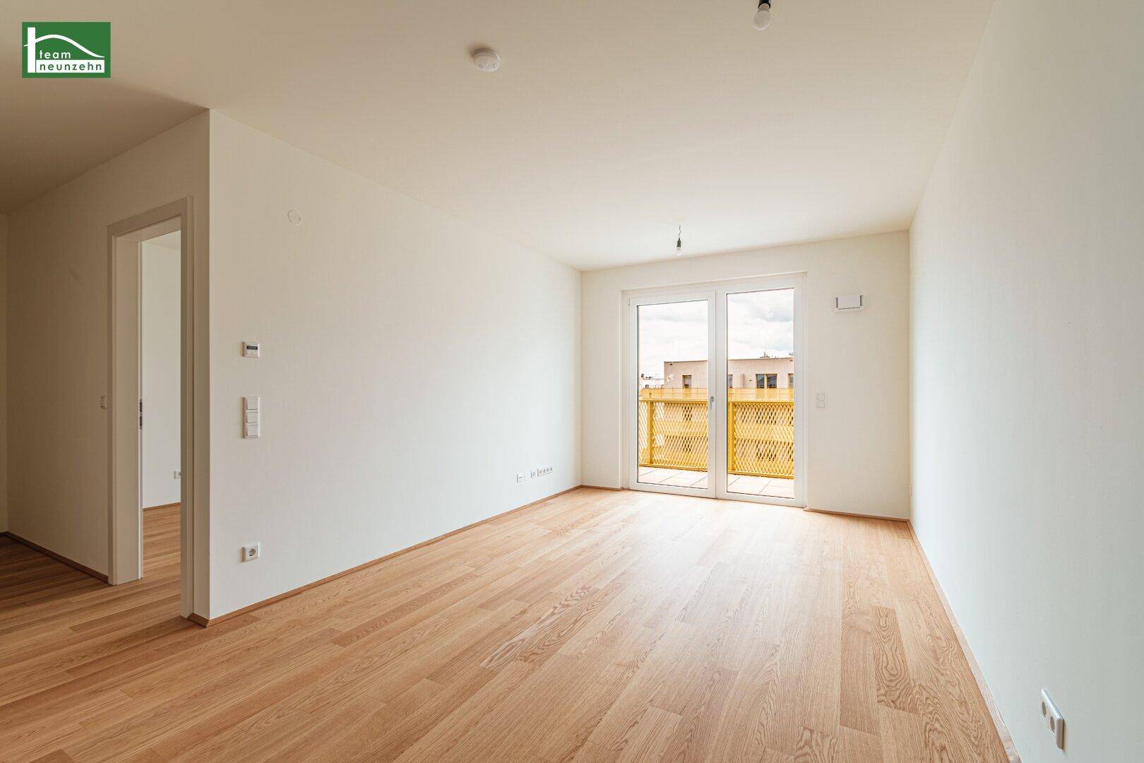 Geräumiger, heller Raum mit Holzboden und breitem Glaszugang zu einem Balkon.