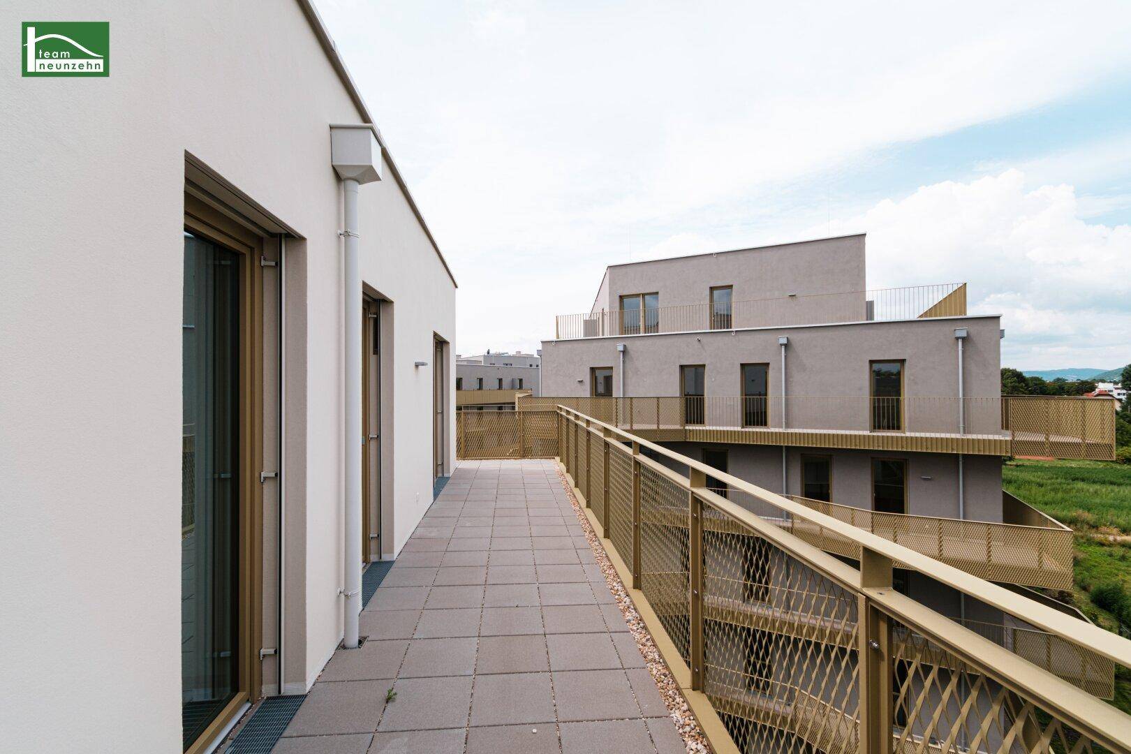Langer Balkon mit Fliesenboden und Blick auf die umliegende Bebauung und Natur.