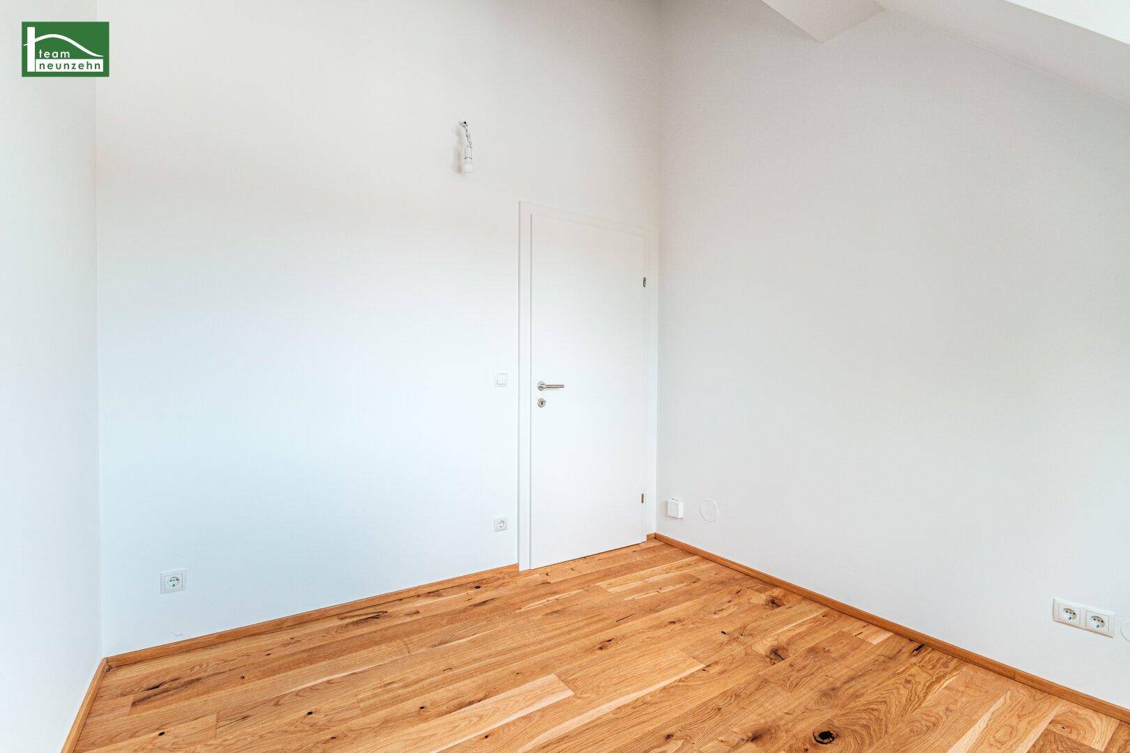 Leeres Zimmer im Dachgeschoss mit Holzboden, weißen Wänden und Tür.