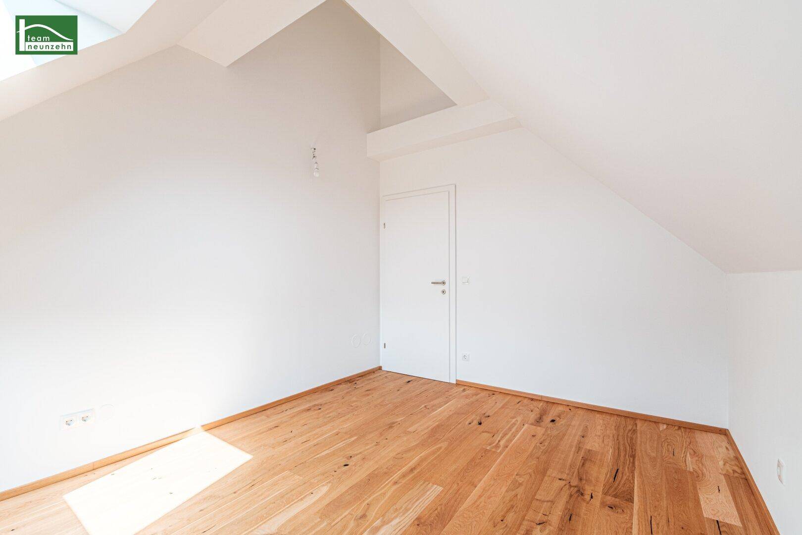 Leeres Zimmer im Dachgeschoss mit Holzboden, weiß gestrichenen Wänden und Tür.