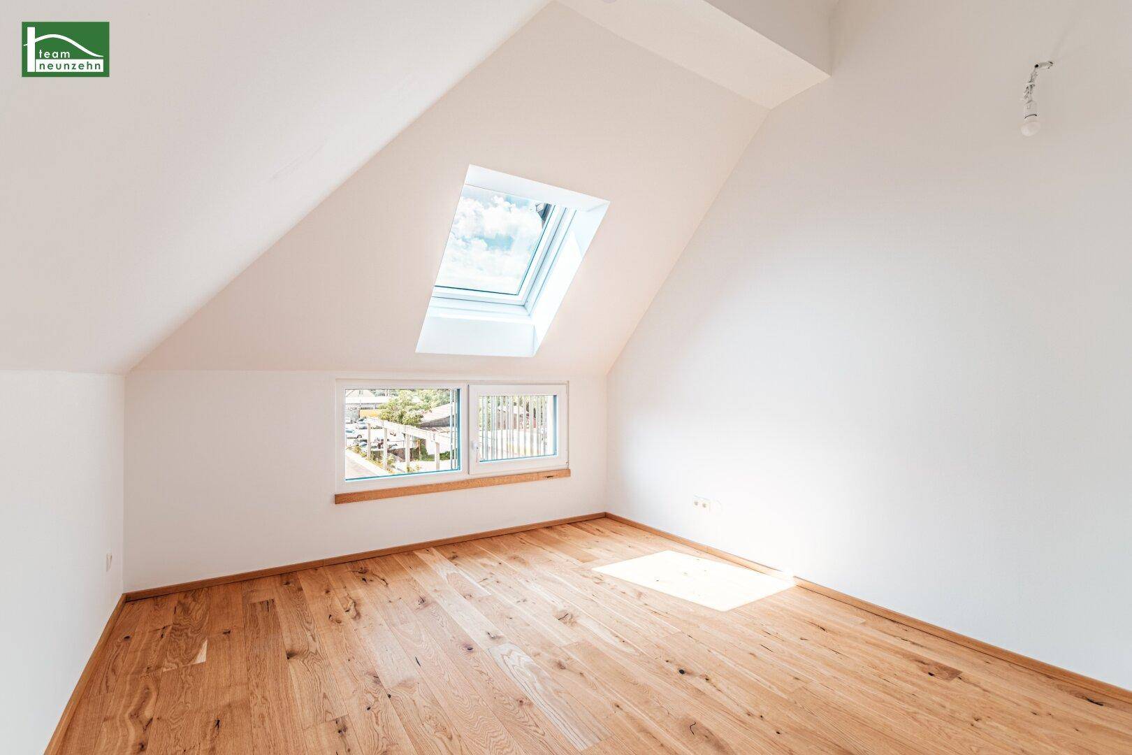 Helles Zimmer im Dachgeschoss mit Holzboden, Dachfenster und schrägen Wänden.