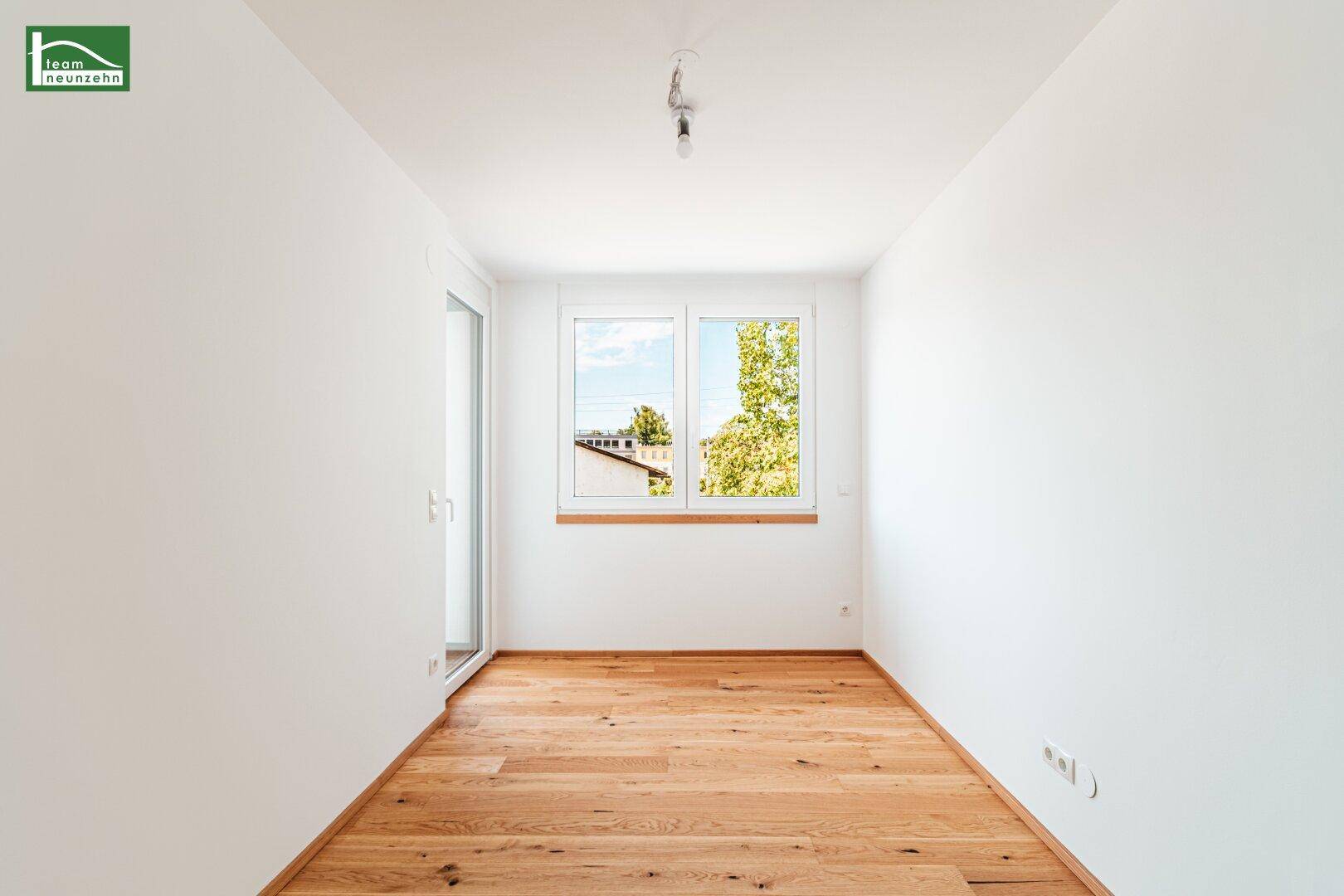 Helles Zimmer mit Holzboden und Zugang zu einem Balkon, bietet viel natürliches Licht.