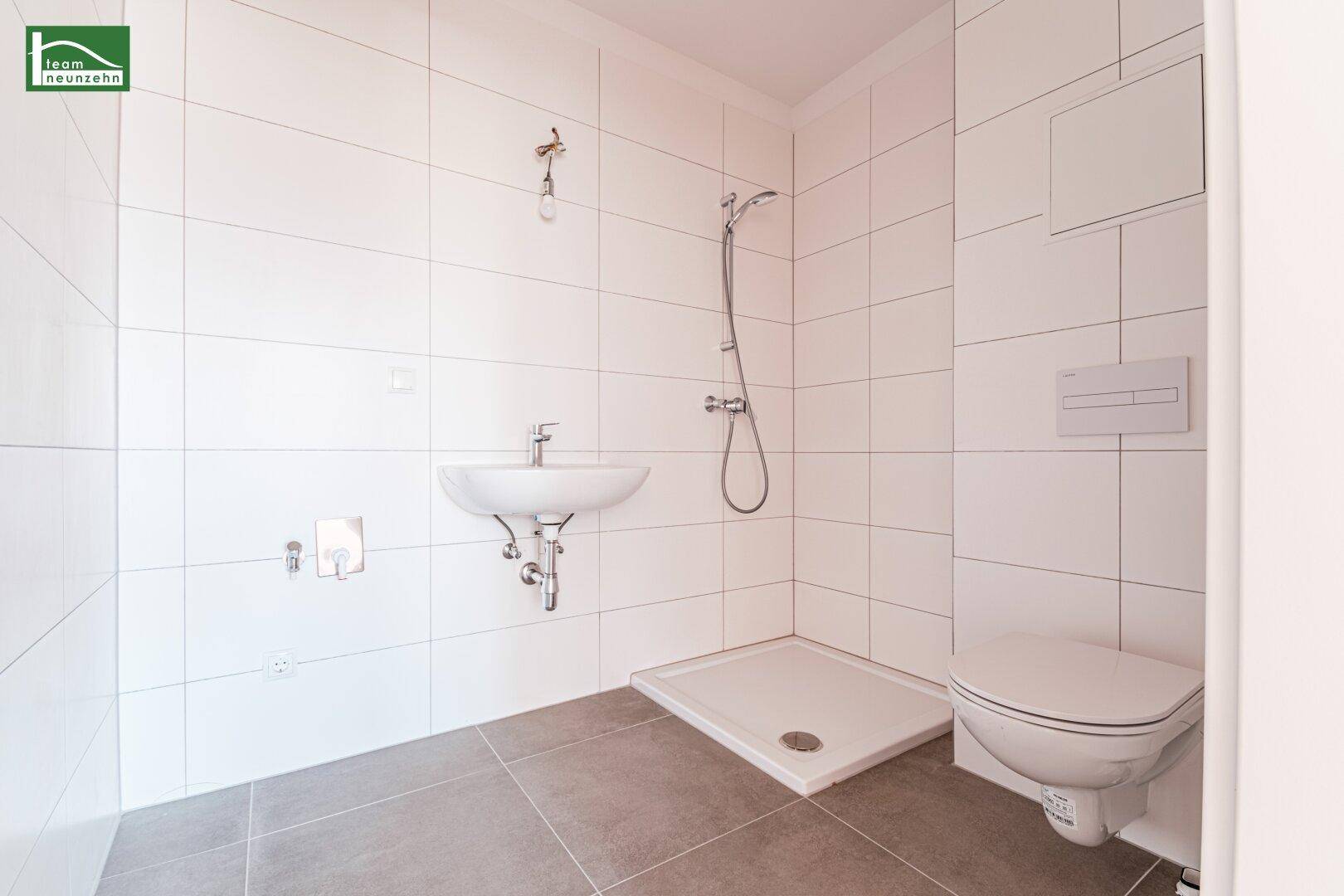 Modernes Badezimmer mit weißen Fliesen, Dusche und wandhängendem WC, in neuwertigem Zustand.