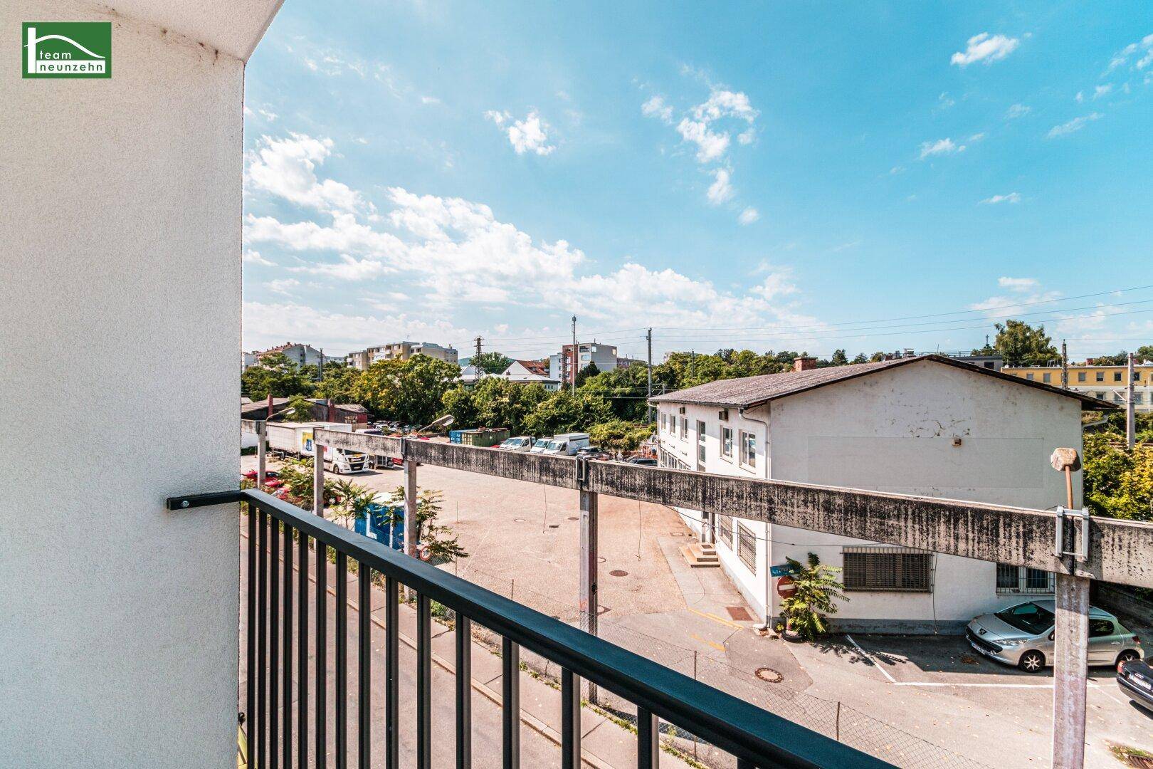 Balkon mit weitem Blick über die Dächer der Stadt und grüne Bäume im Hintergrund.