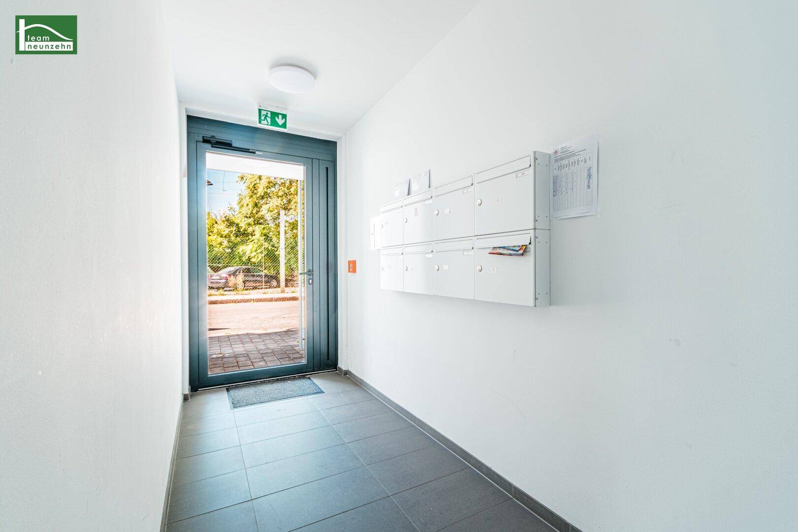 Eingangsbereich mit Briefkästen und einer Glastür, die viel Tageslicht hereinlässt.