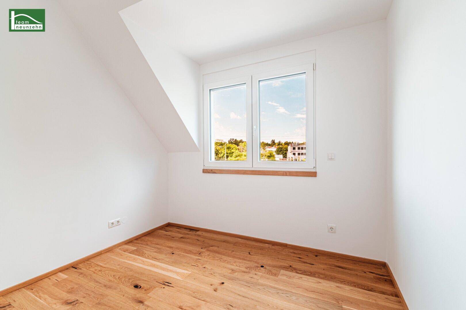 Helles Schlafzimmer im Dachgeschoss mit Holzboden und großem Fenster mit Blick ins Grüne.
