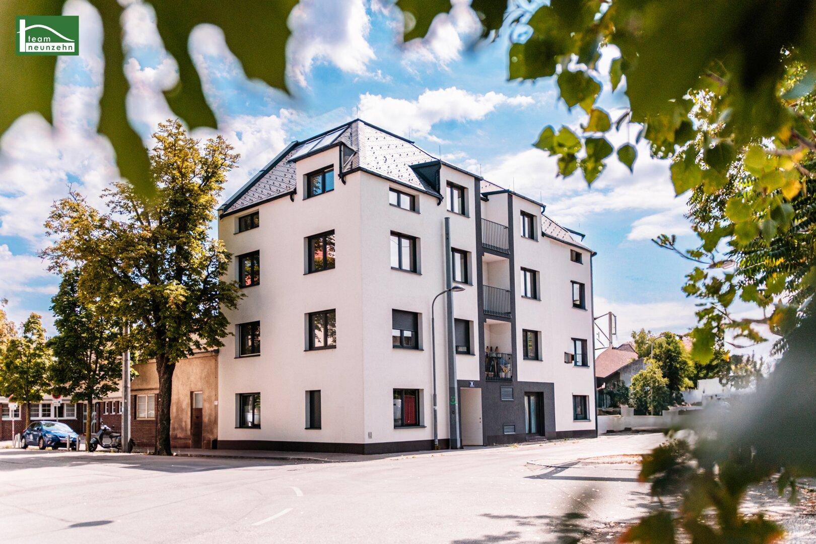 Modernes Mehrfamilienhaus mit weißer Fassade und dunklen Akzenten unter blauem Himmel.