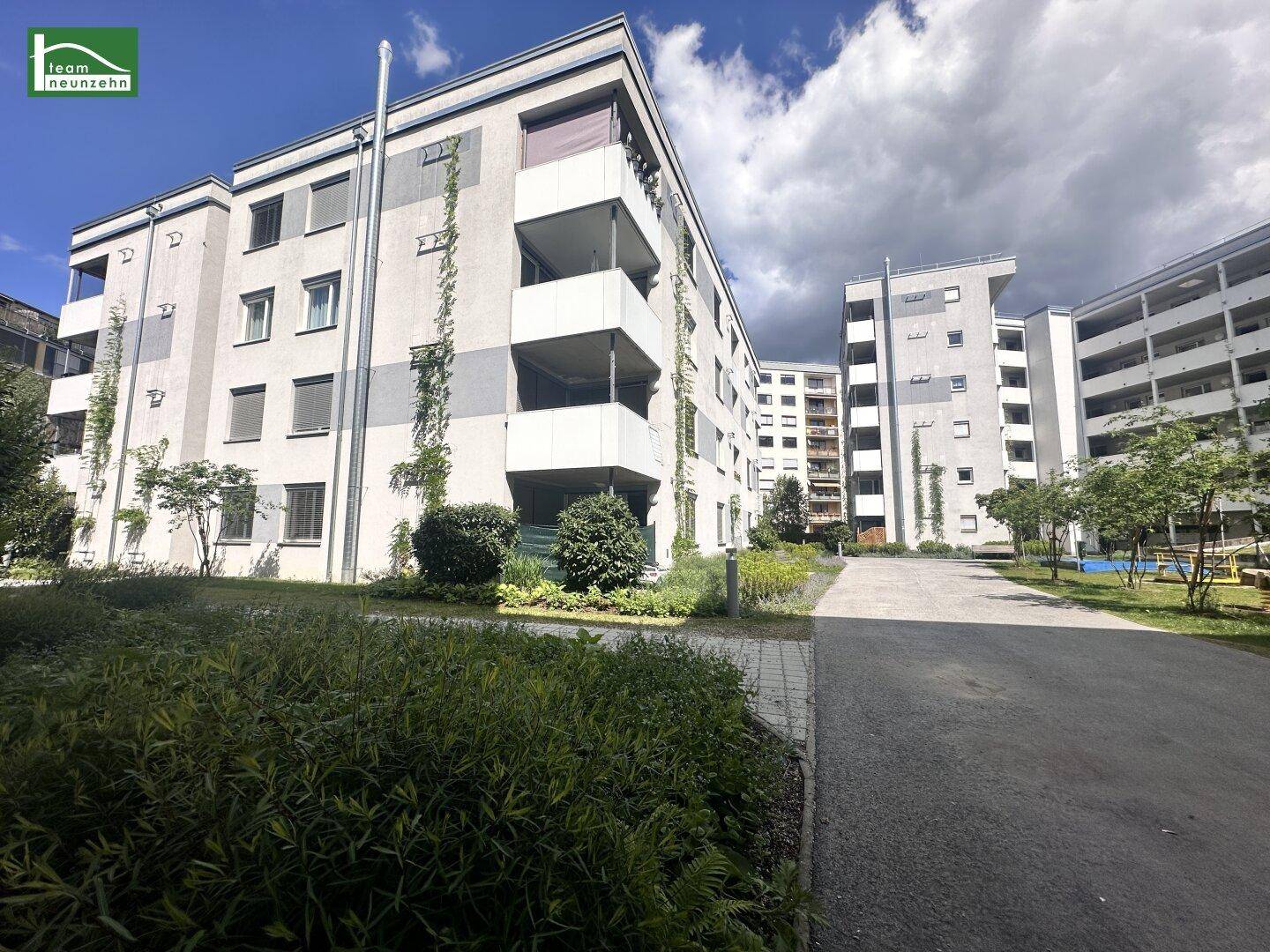 Mehrfamilienhäuser mit Balkonen und begrünten Außenbereichen unter einem bewölkten Himmel.