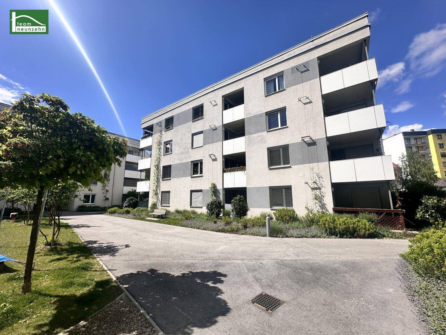 Modernes Mehrfamilienhaus mit Balkonen und gepflegter Außenanlage unter blauem Himmel.