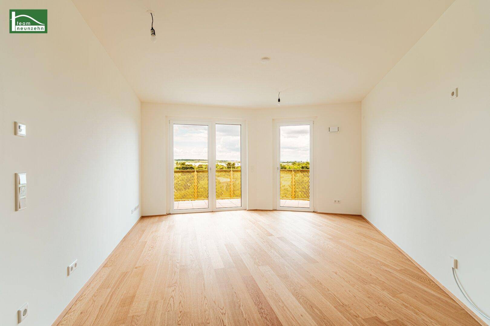 Geräumiger, heller Raum mit Holzboden und zwei großen Fenstertüren zum Außenbereich.