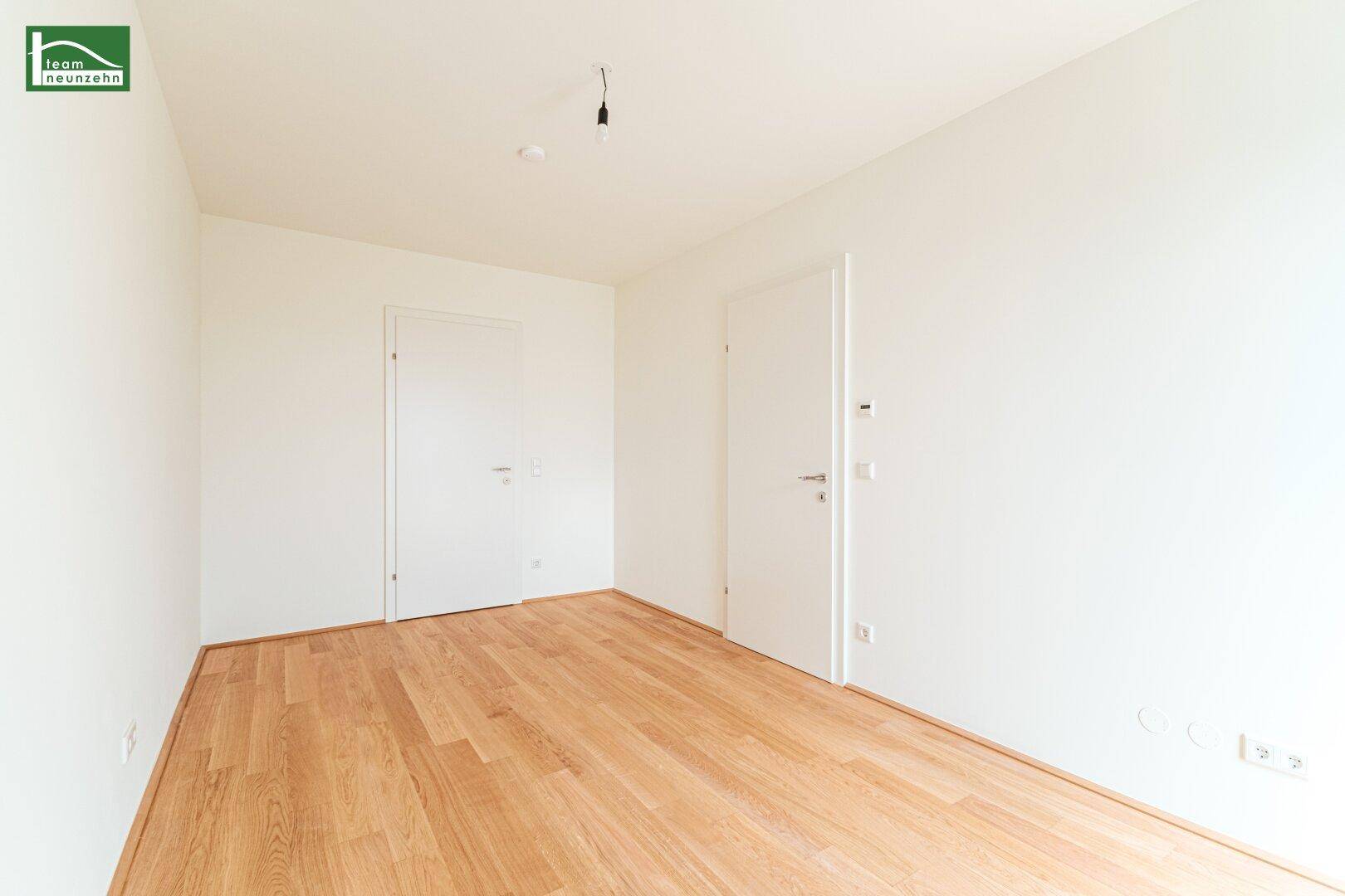 Leeres Zimmer mit hellem Holzparkett und zwei weißen Türen, bietet vielseitige Nutzungsmöglichkeiten.