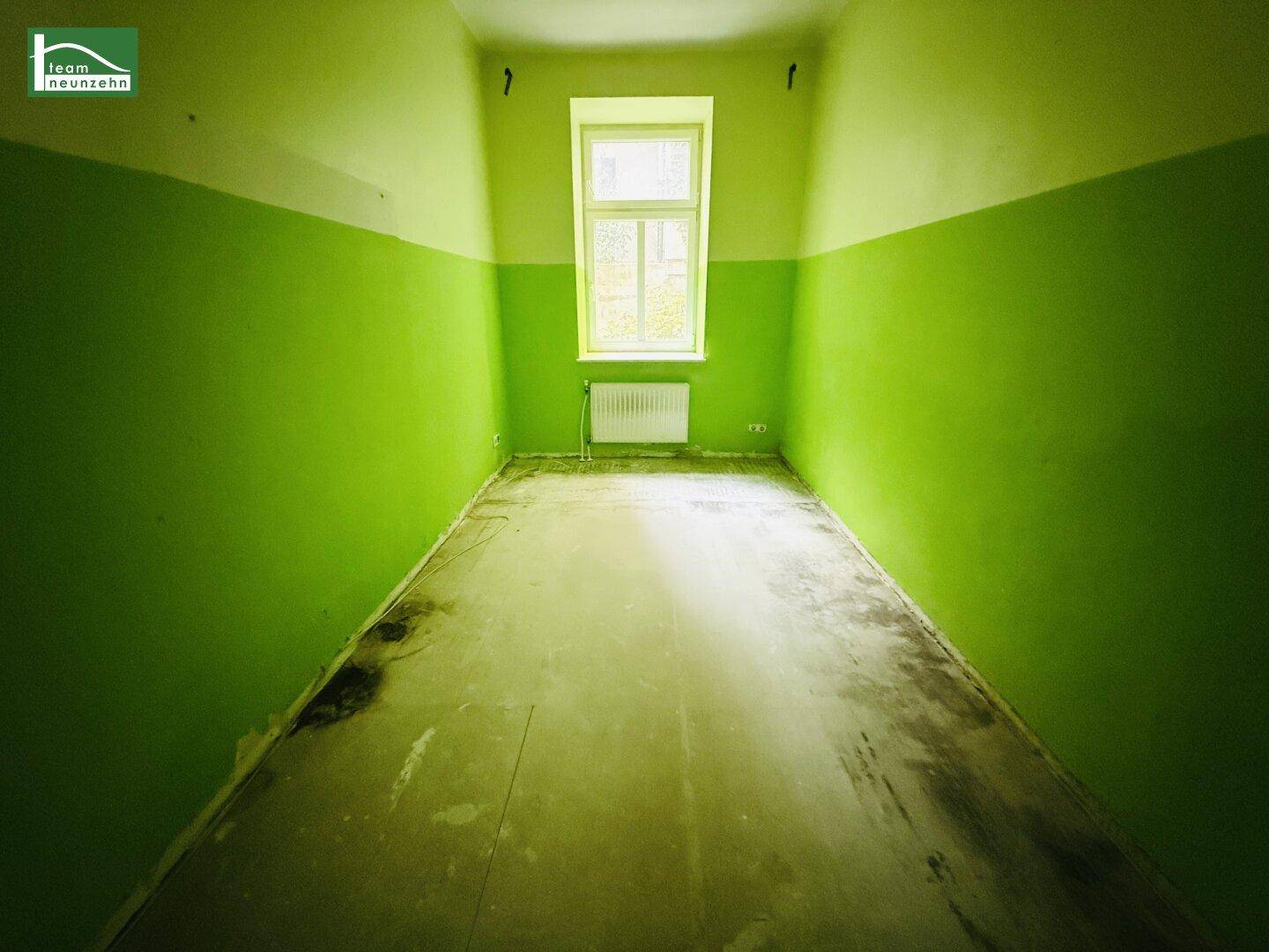 Leerer Raum mit auffälligen grünen Wänden und einem Fenster, das Licht hereinlässt.