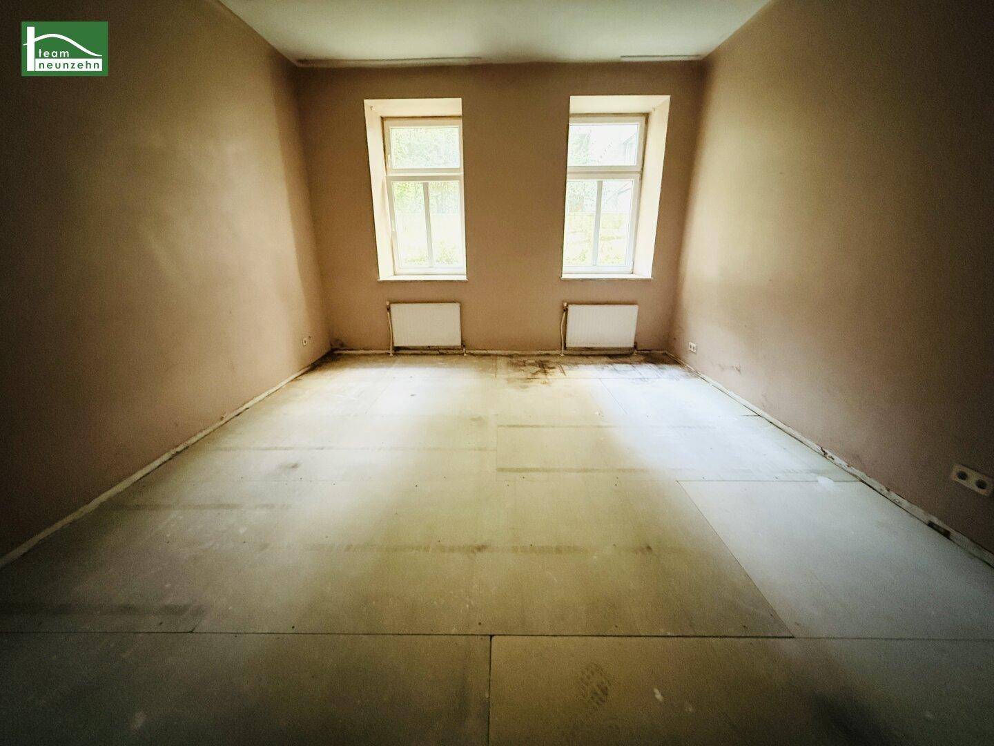 Leerer Raum mit zwei Fenstern und Heizkörpern, bereit für die Renovierung.
