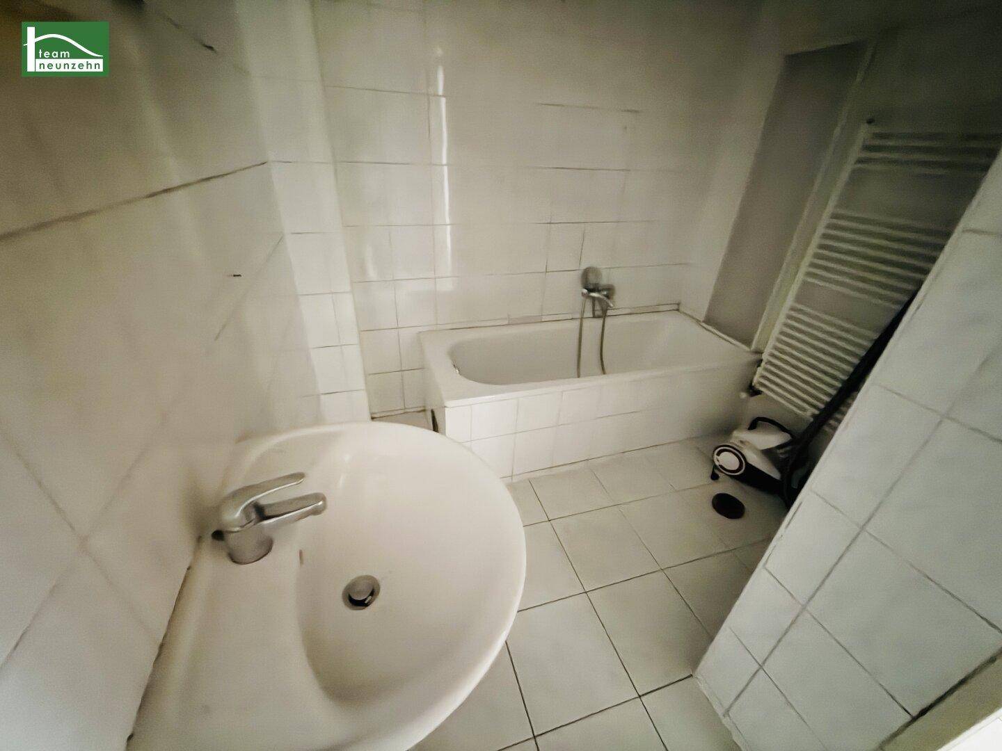 Badezimmer mit Badewanne, Waschbecken und gefliestem Boden, bereit zur Modernisierung.
