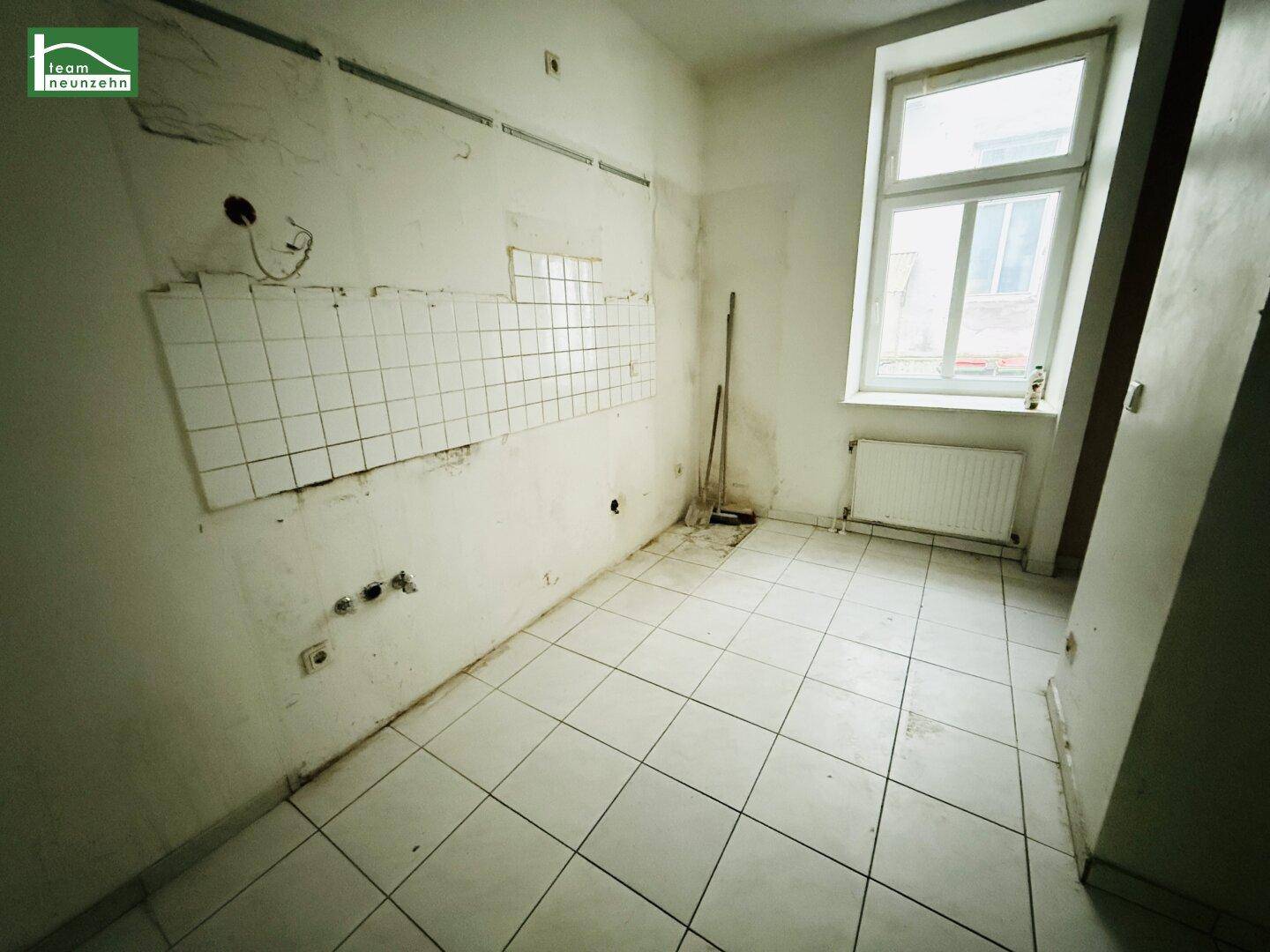 Leere Küche mit Fliesenboden und Fenster, bereit für den Einbau neuer Möbel.